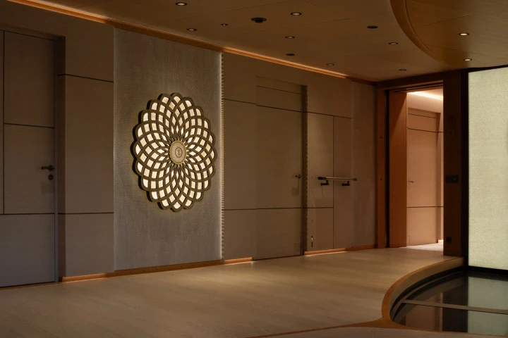 A circular openwork medallion glowing on a wood-panelled wall in a refined corridor, Private Mega Yacht.