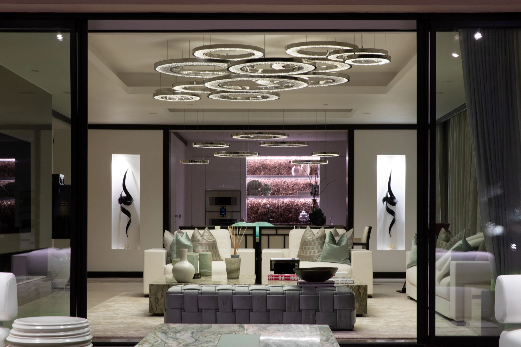 Modern living room with circular ring chandeliers above white sofas and artwork.