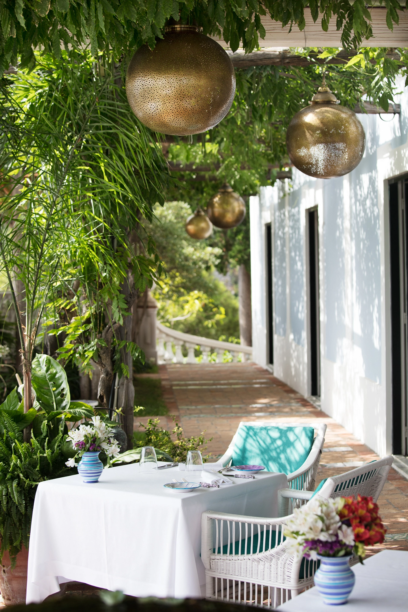 Globe pendants above a white-clothed table on a pergola walkway framed by greenery and the sea.