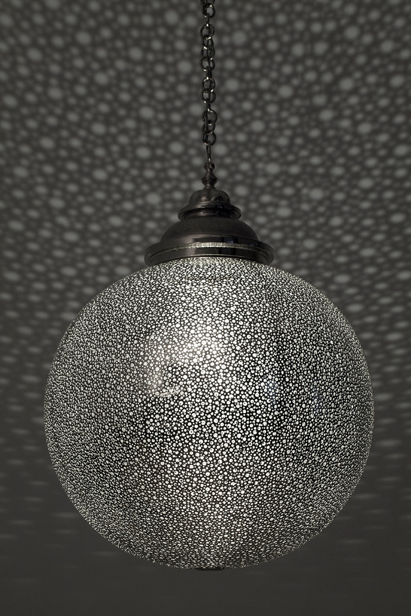 Large pierced-silver globe pendant lit from within, set against a softly dotted grey background.