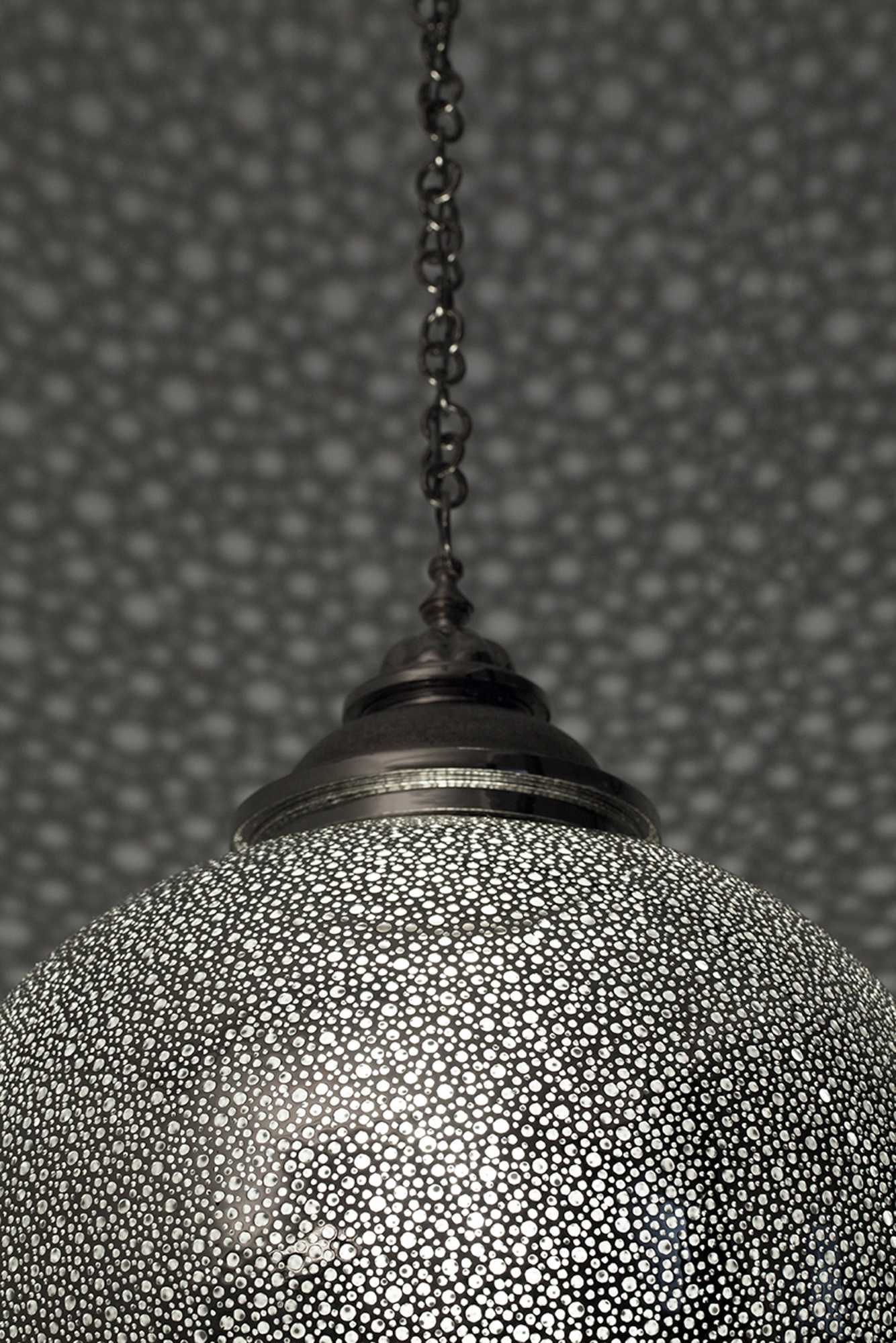 Close-up of the lower hemisphere of a pierced-silver globe pendant, its fine perforations catching light.