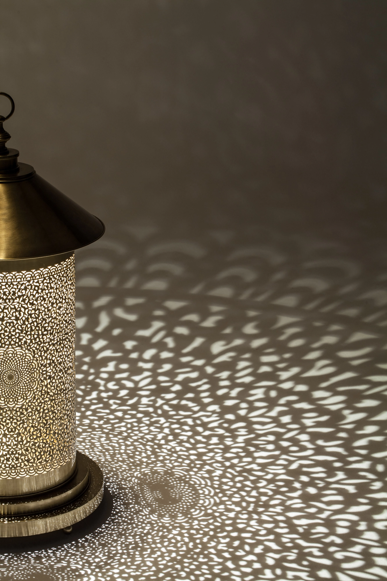 Close-up of a pierced cylindrical floor lamp's base scattering dotted light across the surrounding floor.