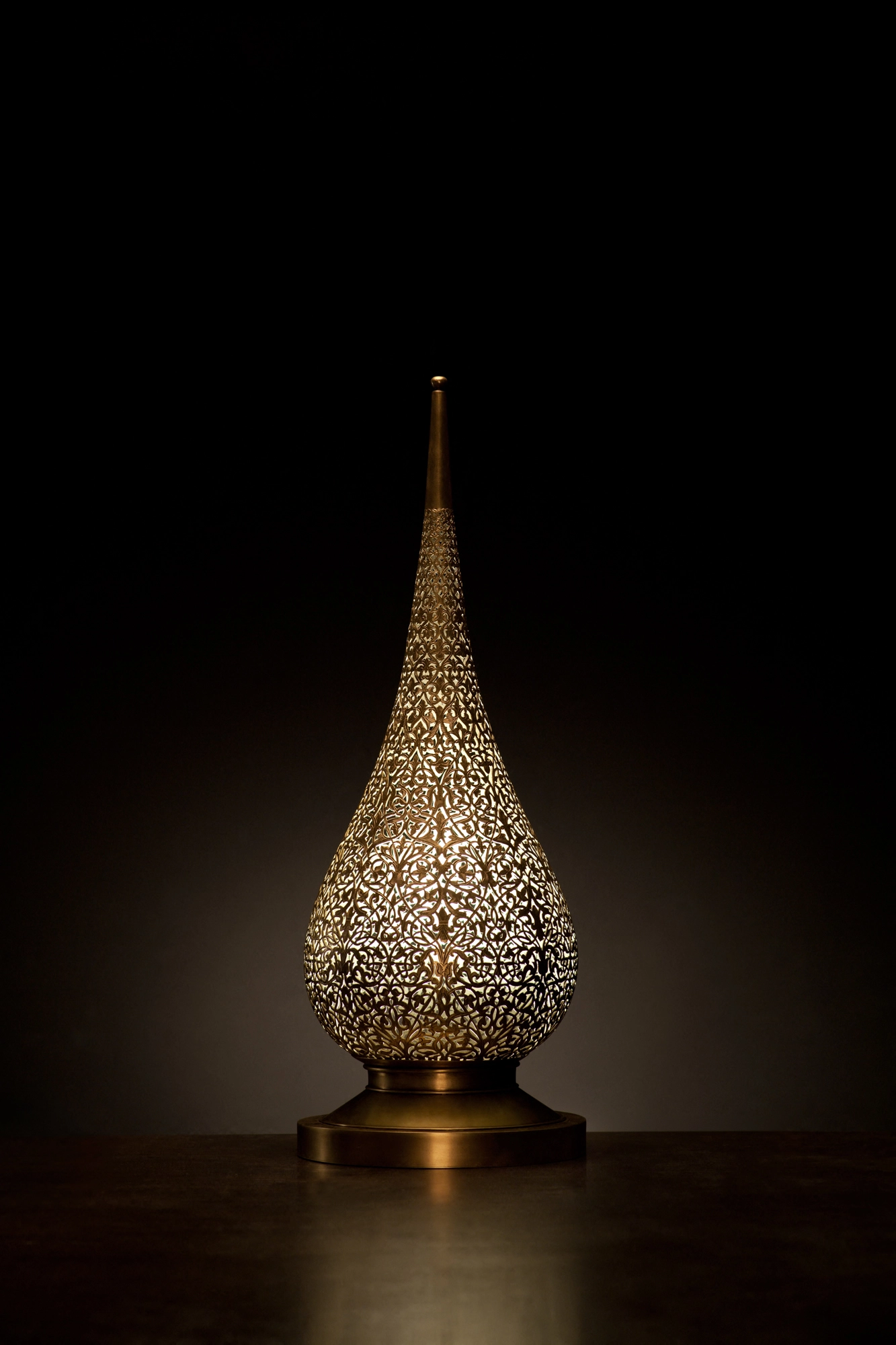 A flame-shaped pierced metal candle holder lit from within, glowing against a dark background.