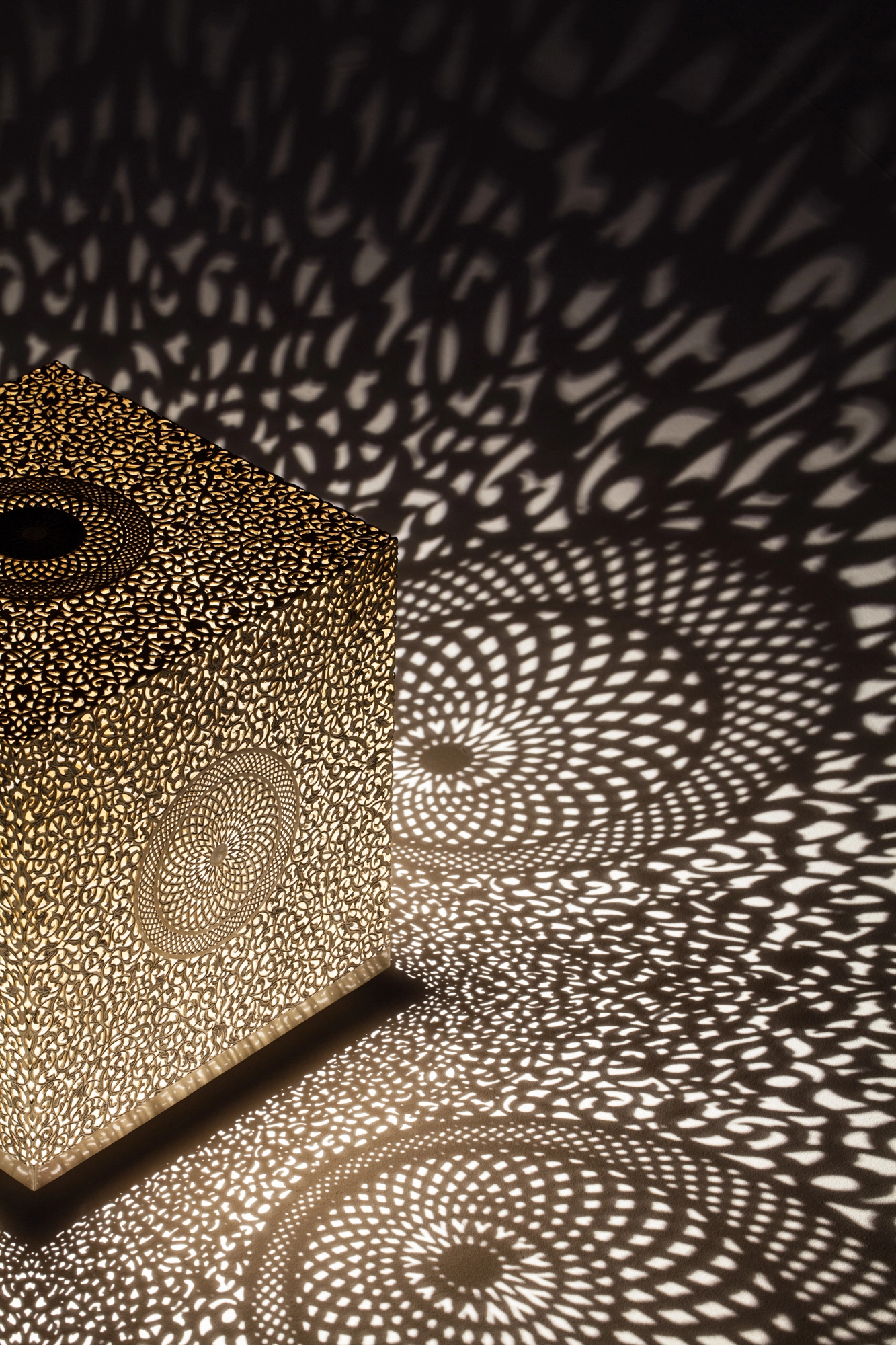 Close-up of a pierced cube lamp casting concentric circles of dotted light across the floor.