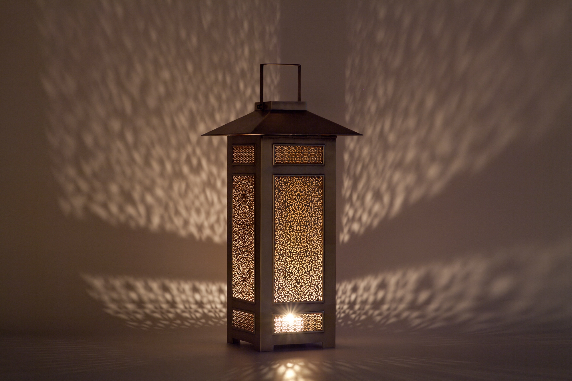 A square lantern with a pagoda-style roof and pierced panels lit from within, scattering dotted light around it.