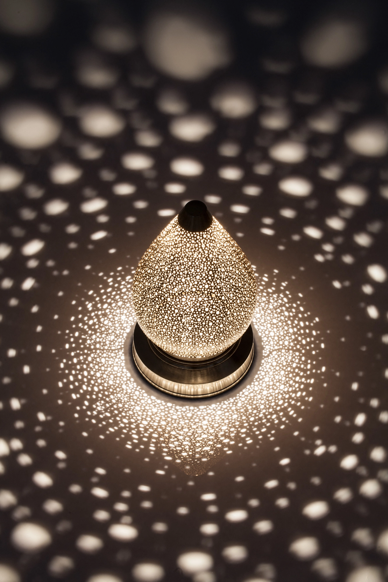 Pierced lotus lamp seen from a high angle, glowing within a dense circular field of light dots.