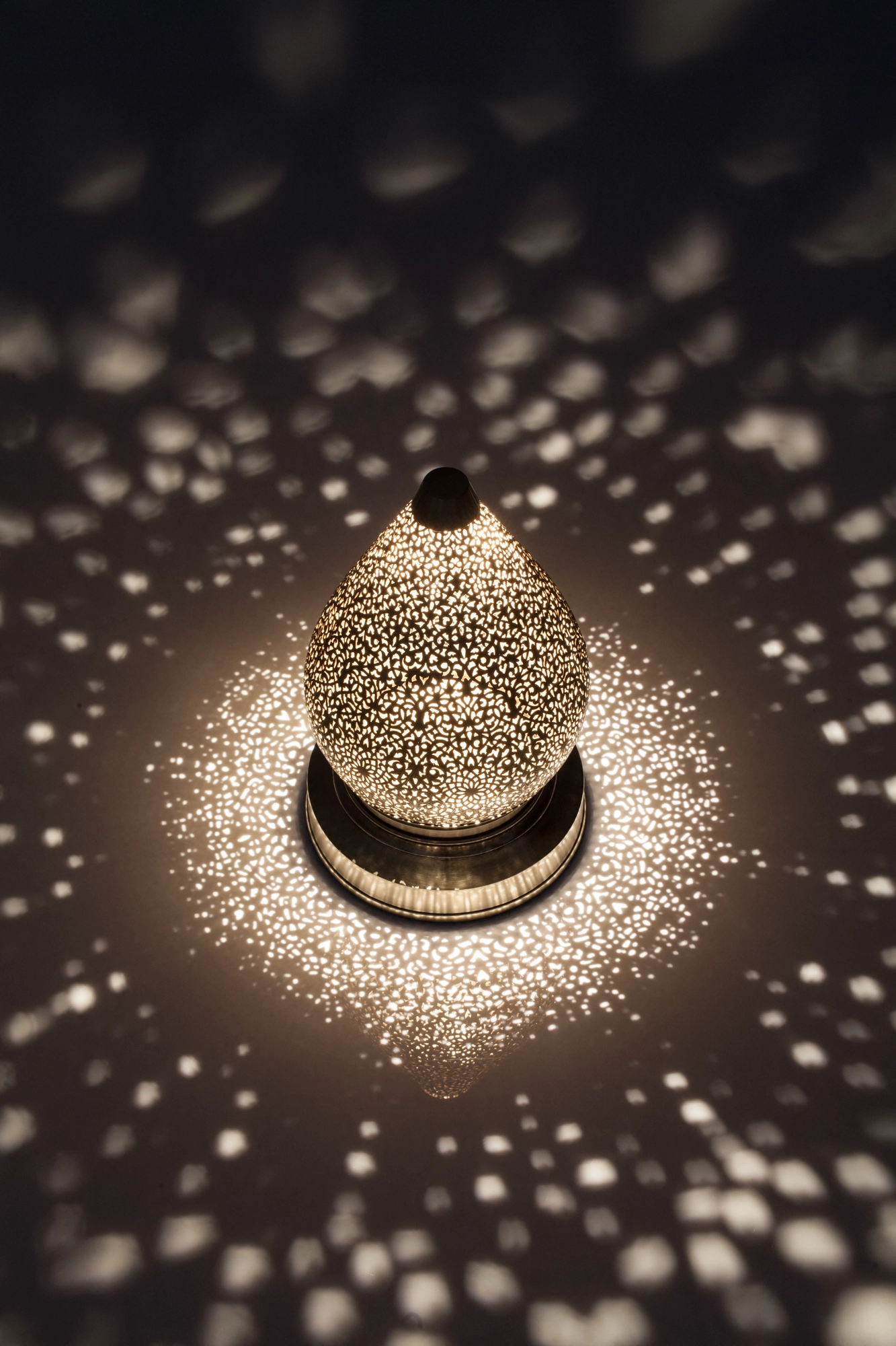 Pierced-brass lotus lamp glowing low on a surface, ringed by a bright burst of scattered light dots.
