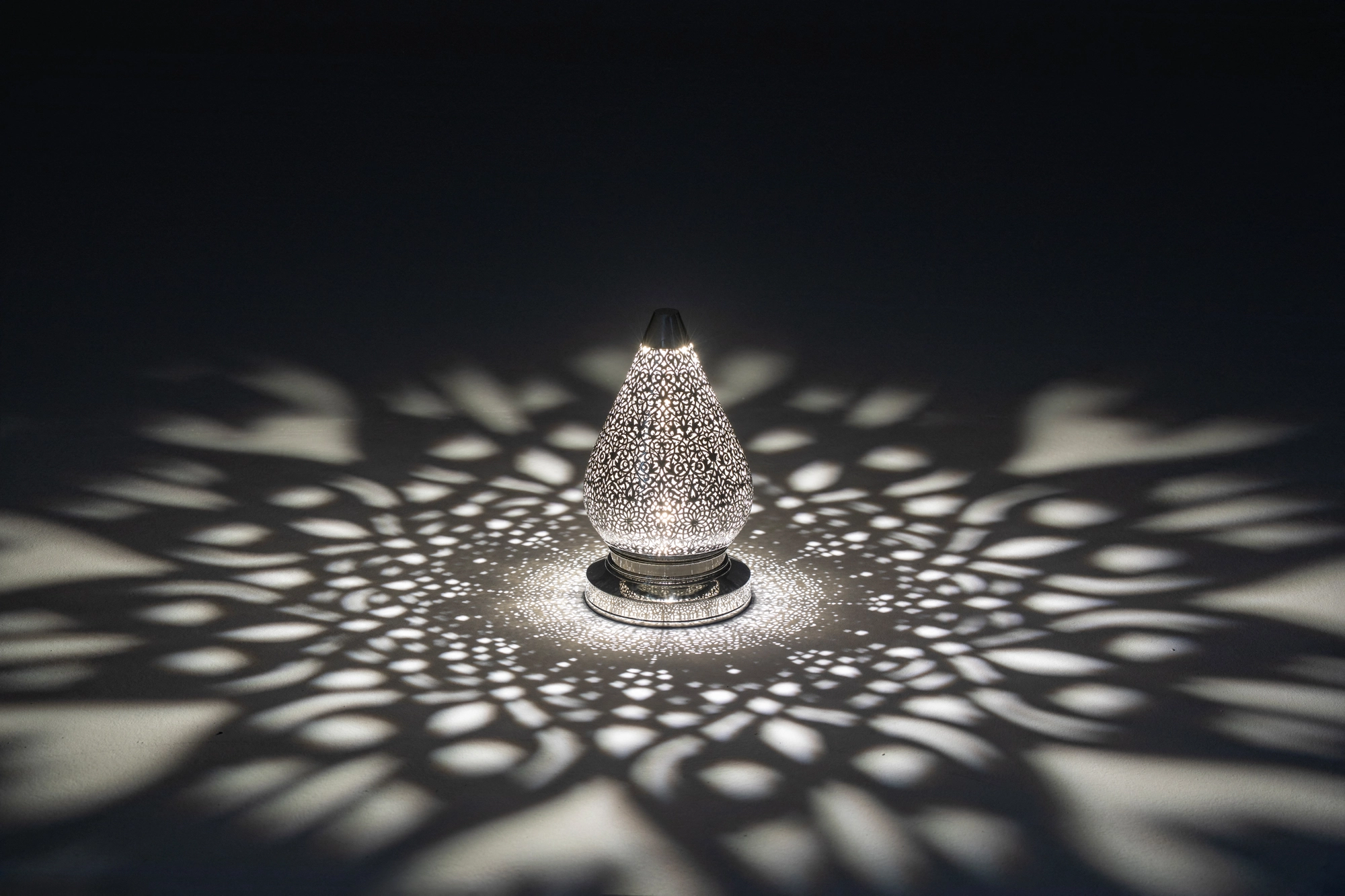 Pierced-brass lotus lamp glowing faintly, throwing a star-shaped pattern of light dots around it.
