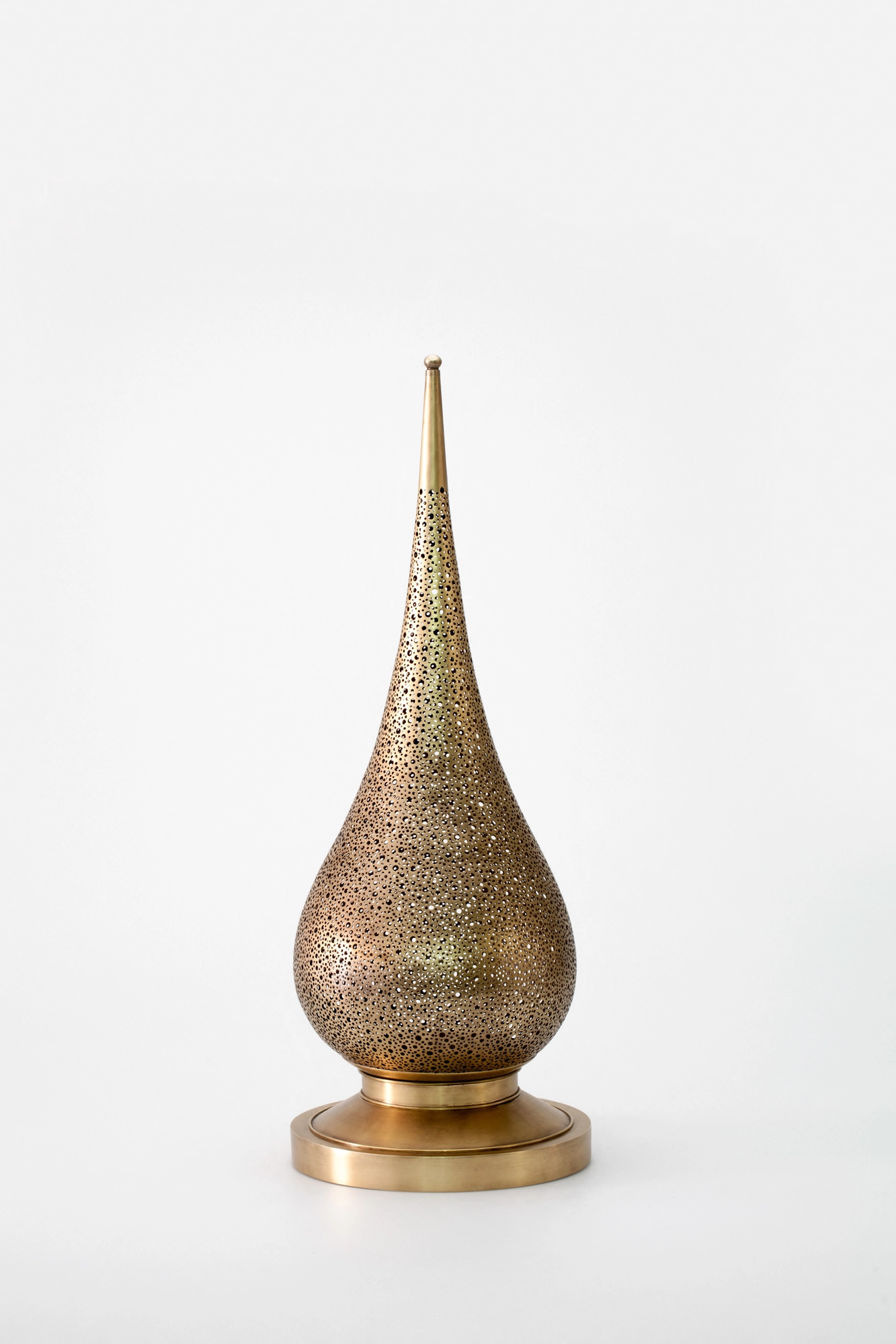 A tall teardrop-shaped pierced metal candle holder on a brass base, photographed unlit against a white background.