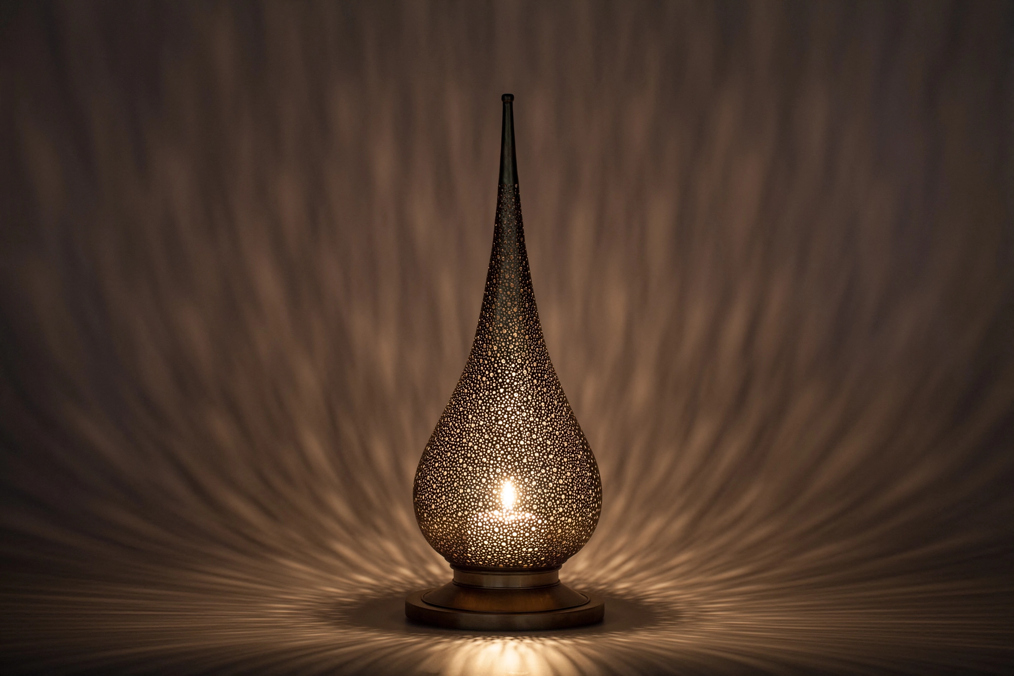 A flame-shaped pierced candle holder lit from within, radiating a warm glow across a dim surface.