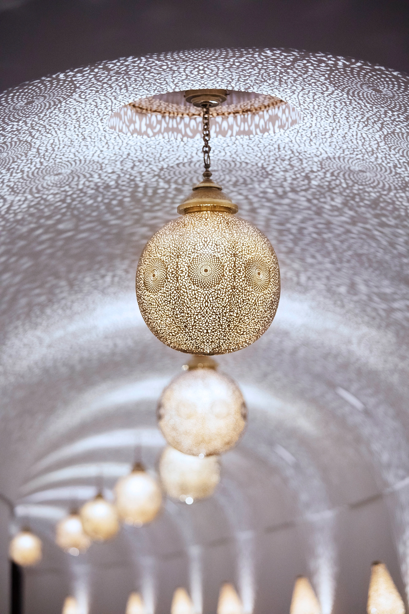 Pierced brass globe pendant beneath a domed pierced ceiling, lit by candlelight.