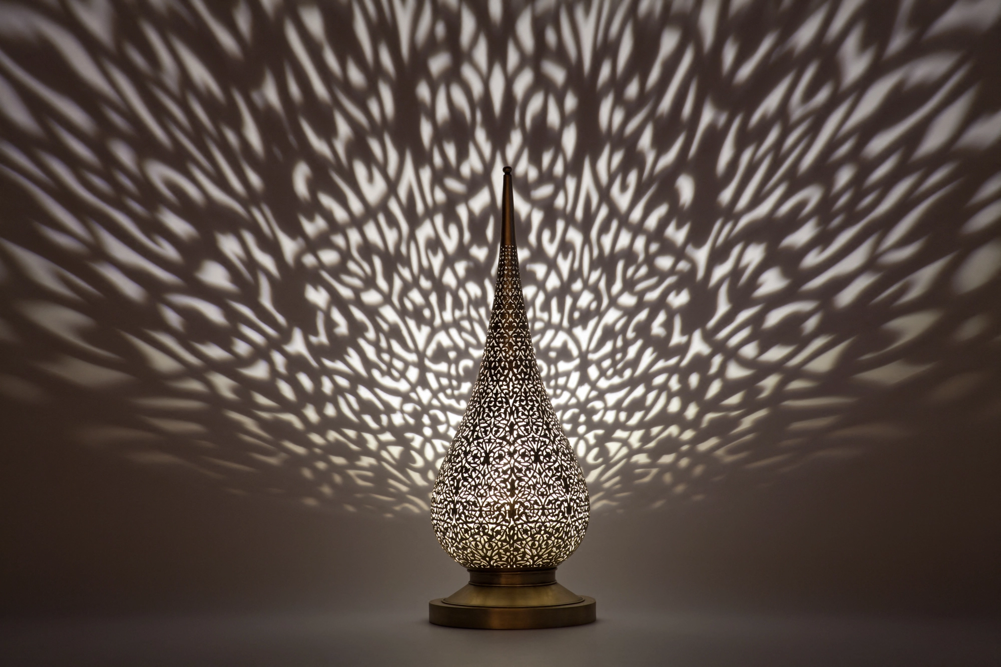 A flame-shaped pierced candle holder casting a broad spray of dappled light across a dark background.