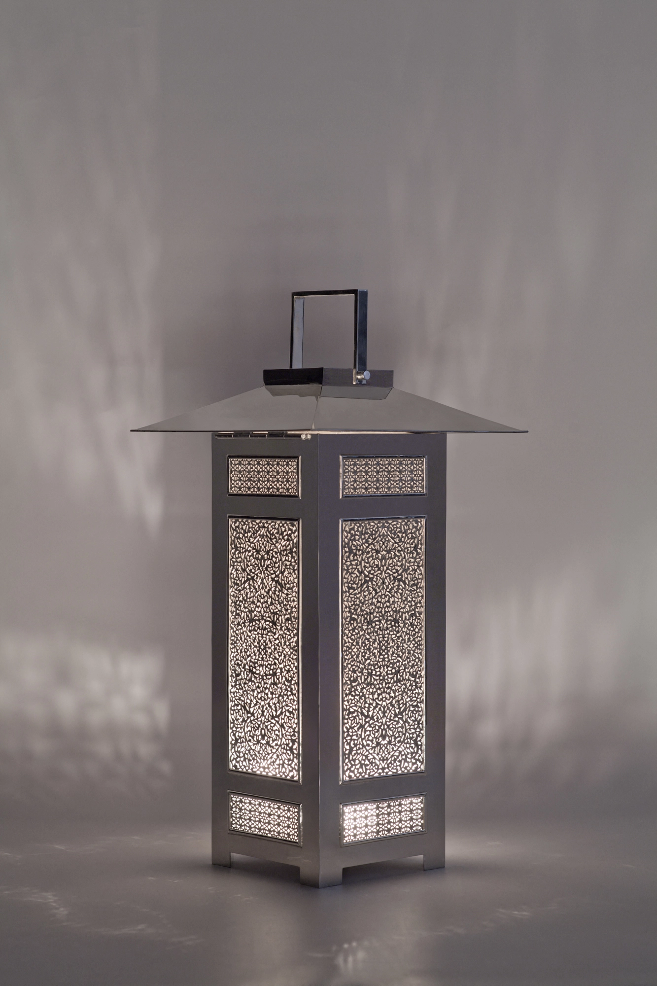 A silver square lantern with a pagoda-style roof and finely pierced panels, against a grey background.