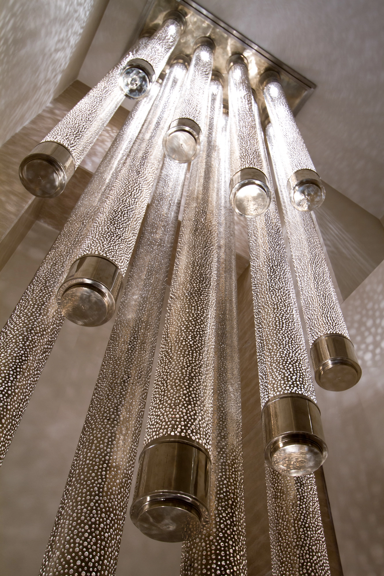 Close-up of clustered cylindrical liquid-light glass tubes hanging vertically, lit and textured along their length.