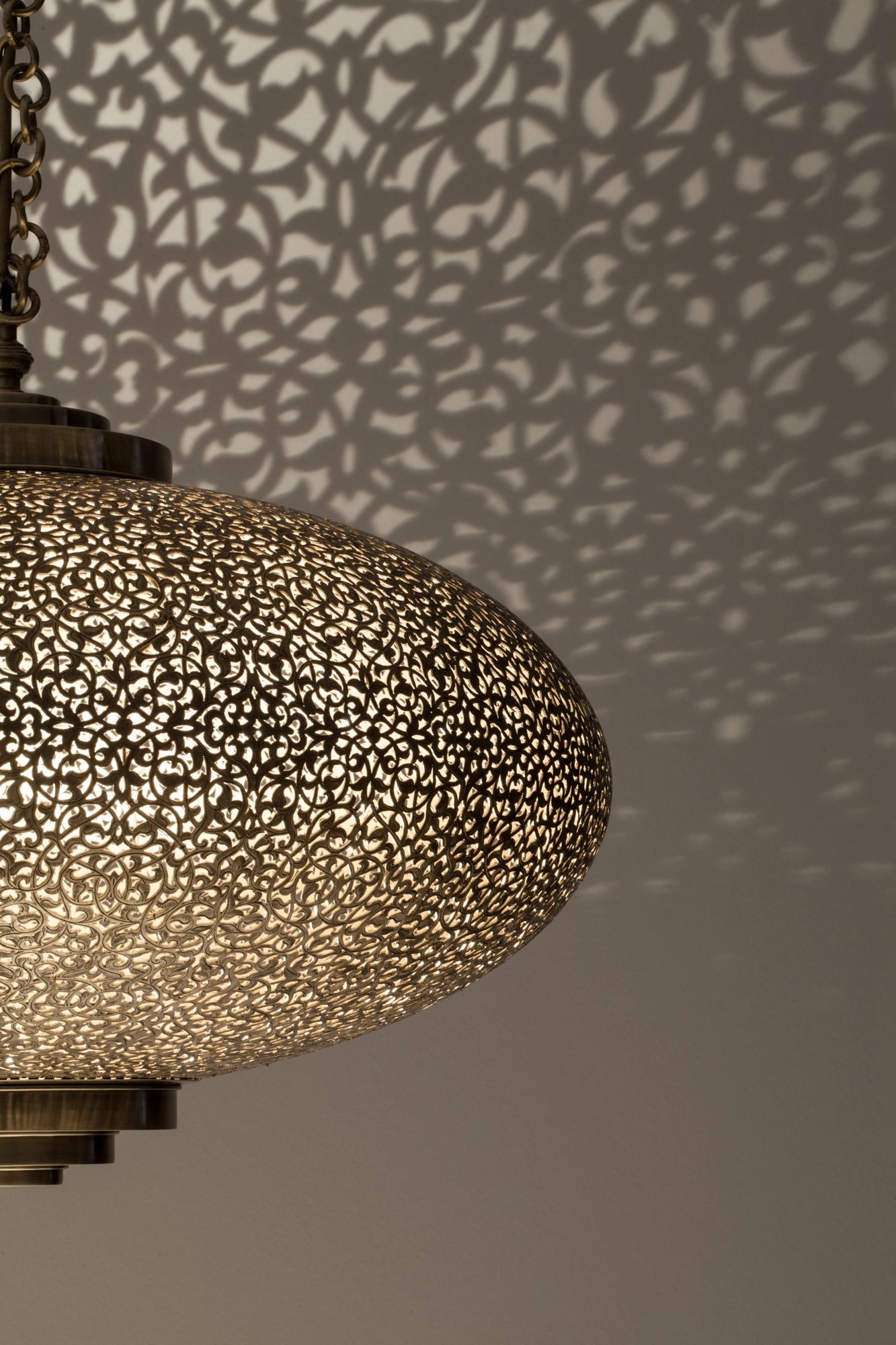Close-up of a pierced-brass squashed-globe pendant, its lower surface dense with glowing perforations.