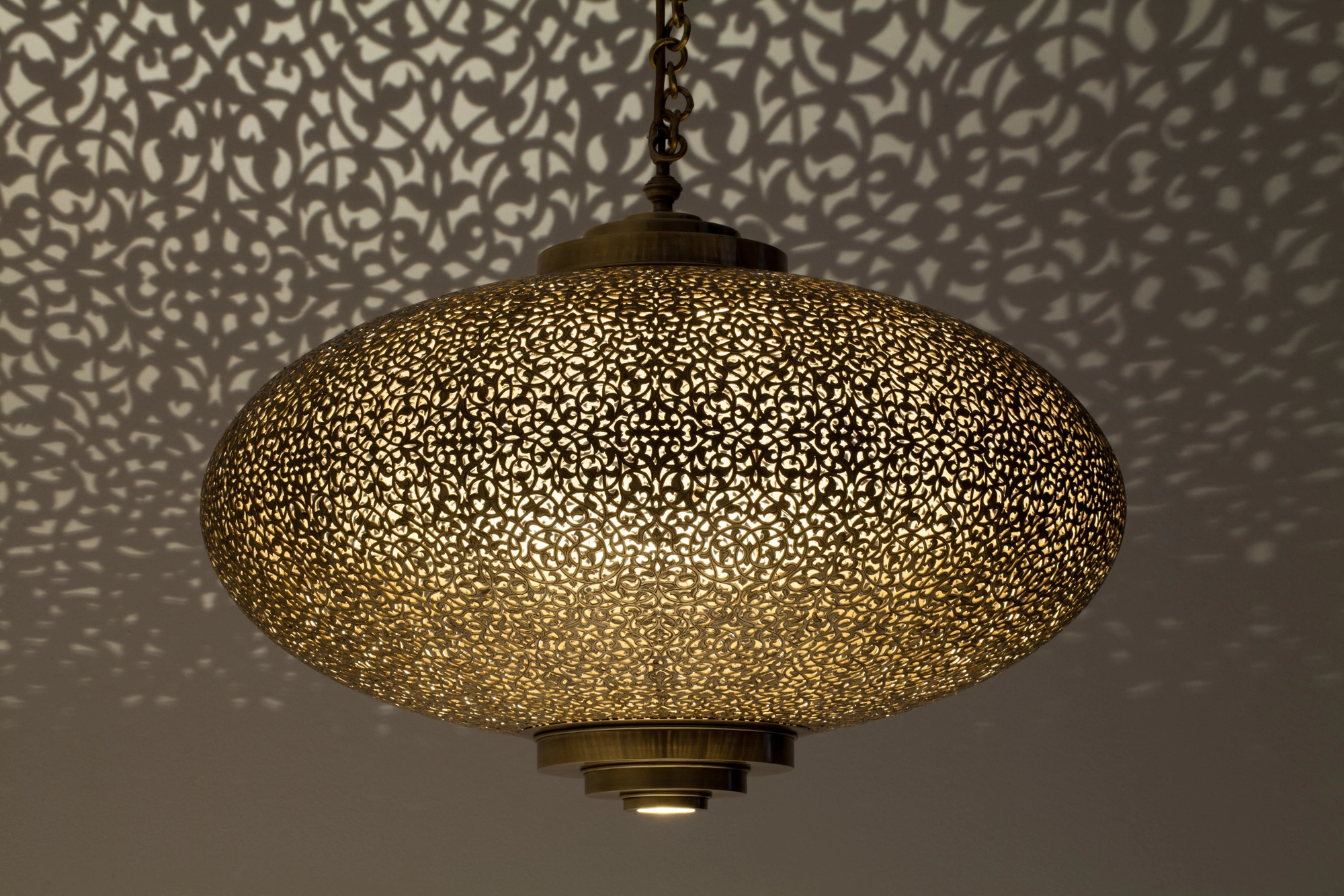 Flattened pierced-brass squashed-globe pendant glowing beneath a ceiling washed with fine light dots.