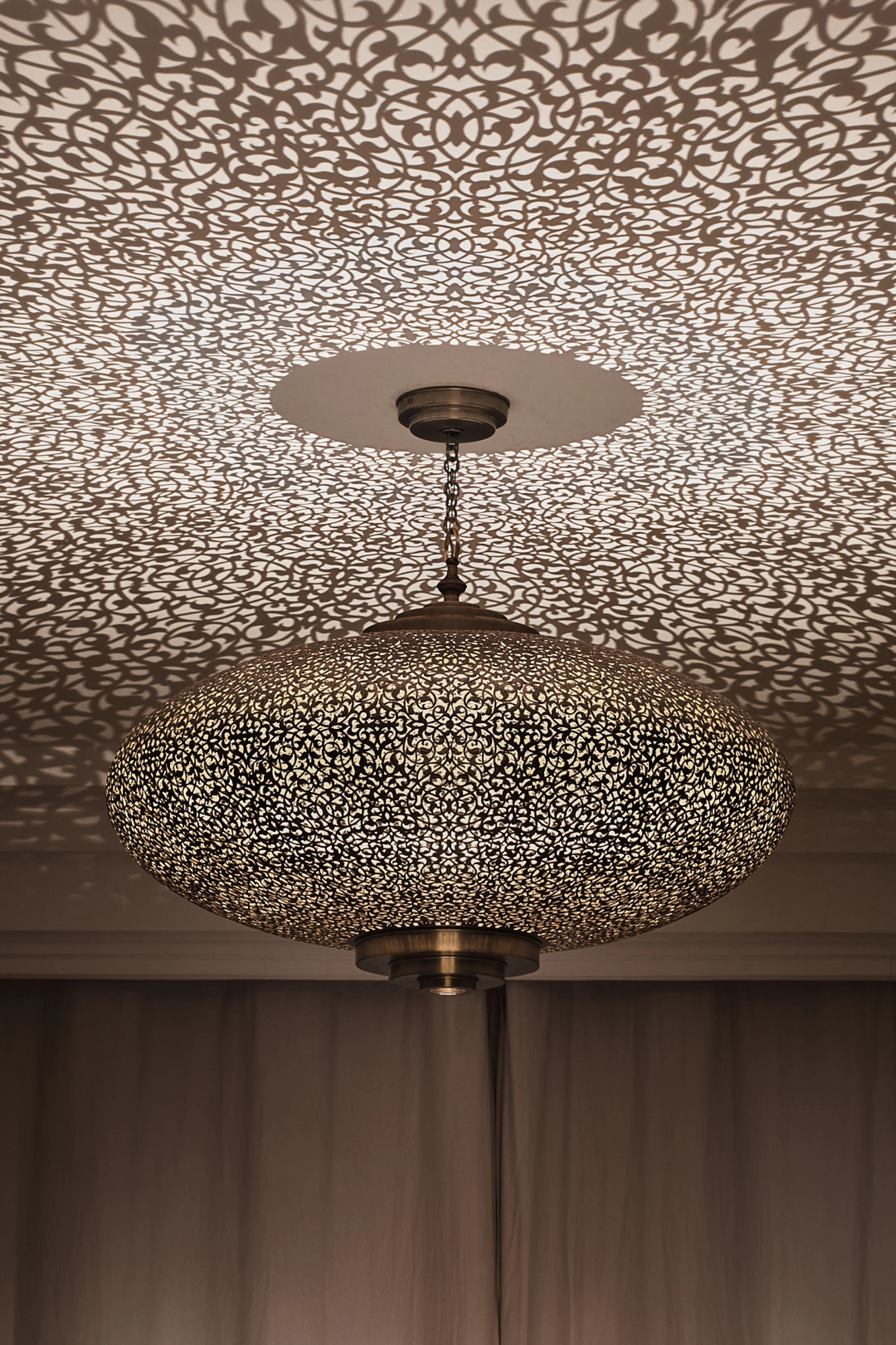 Flattened pierced-brass squashed-globe pendant on a stem, ringed by a dense halo of light dots near the ceiling.