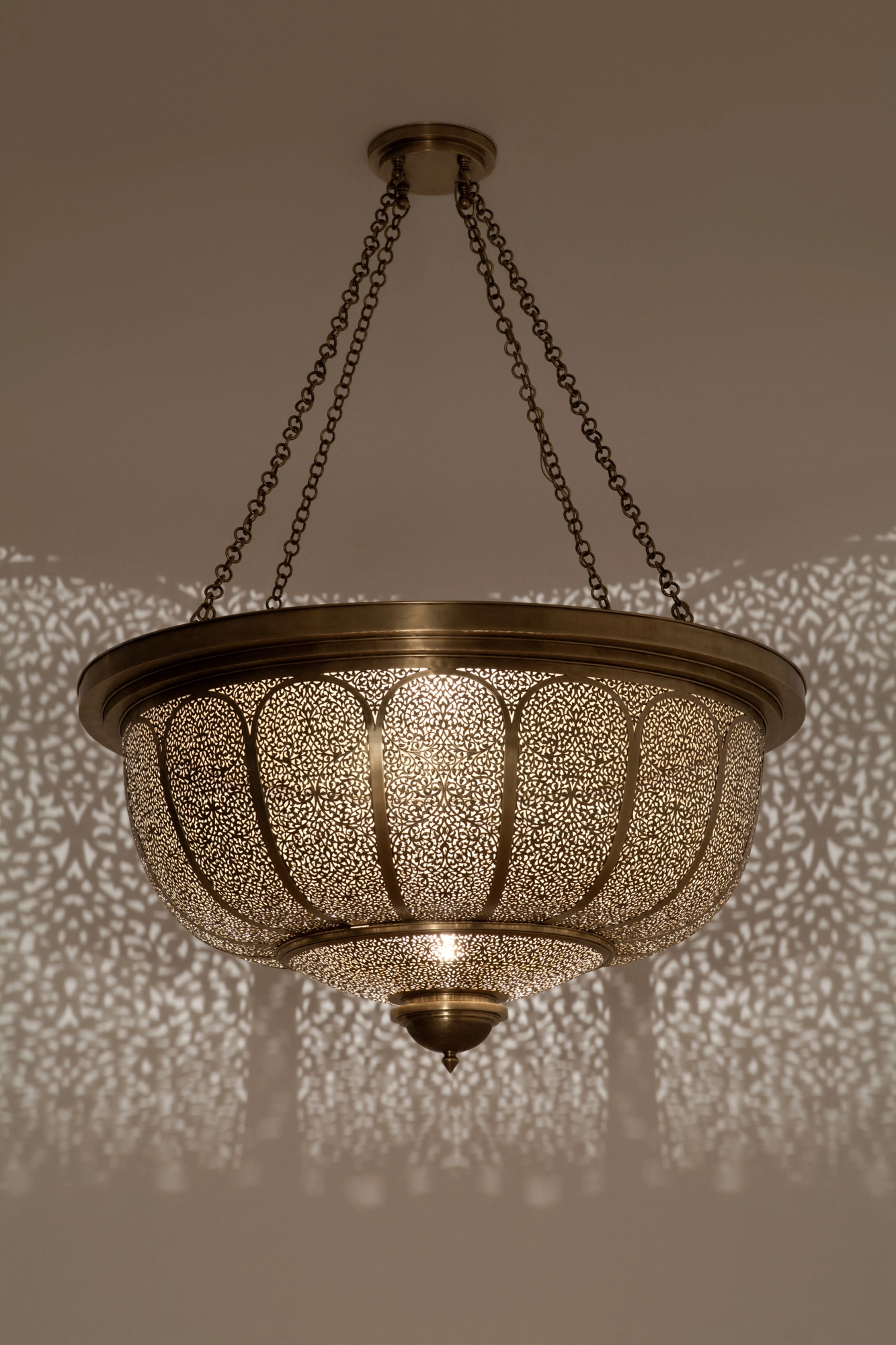 Large pierced-brass bowl pendant suspended on chains, scattering a dense field of light dots on the wall below.