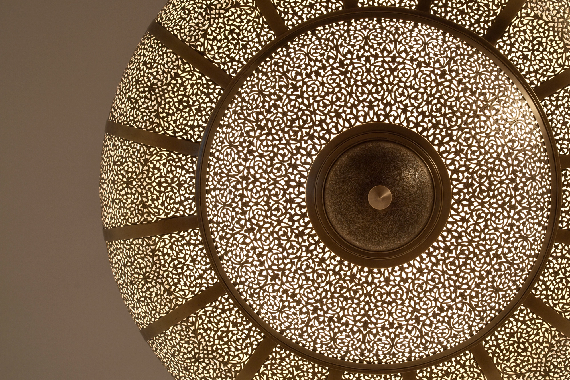Underside of a pierced-brass bowl pendant seen from below, its radial spokes framing a central brass boss.