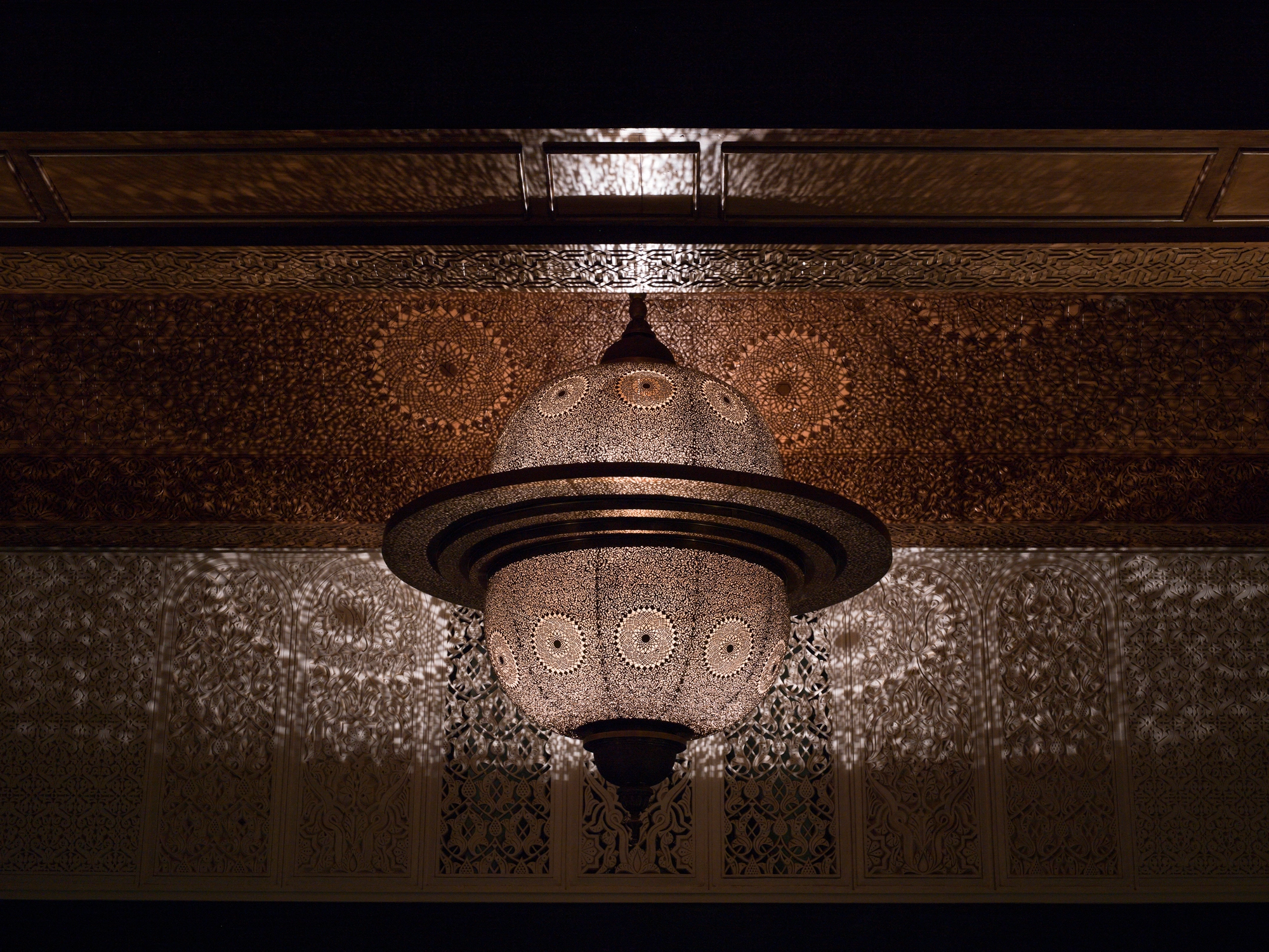 Pierced twin-dome pendant light glowing softly against a dark, richly patterned wall.