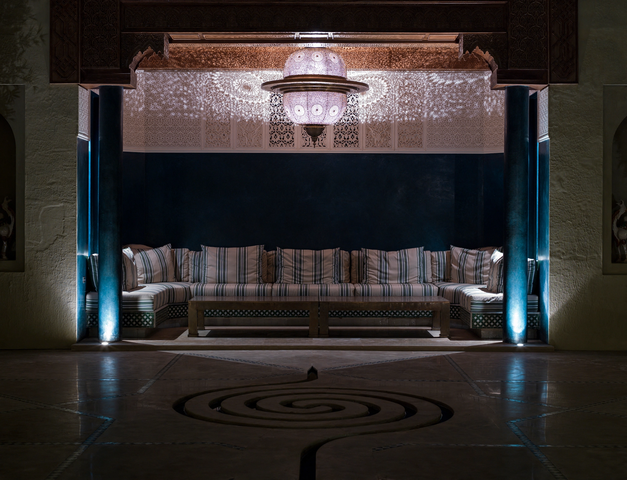 Pierced twin-dome pendant light glowing above a sofa, with a spiral pattern on the dark floor.