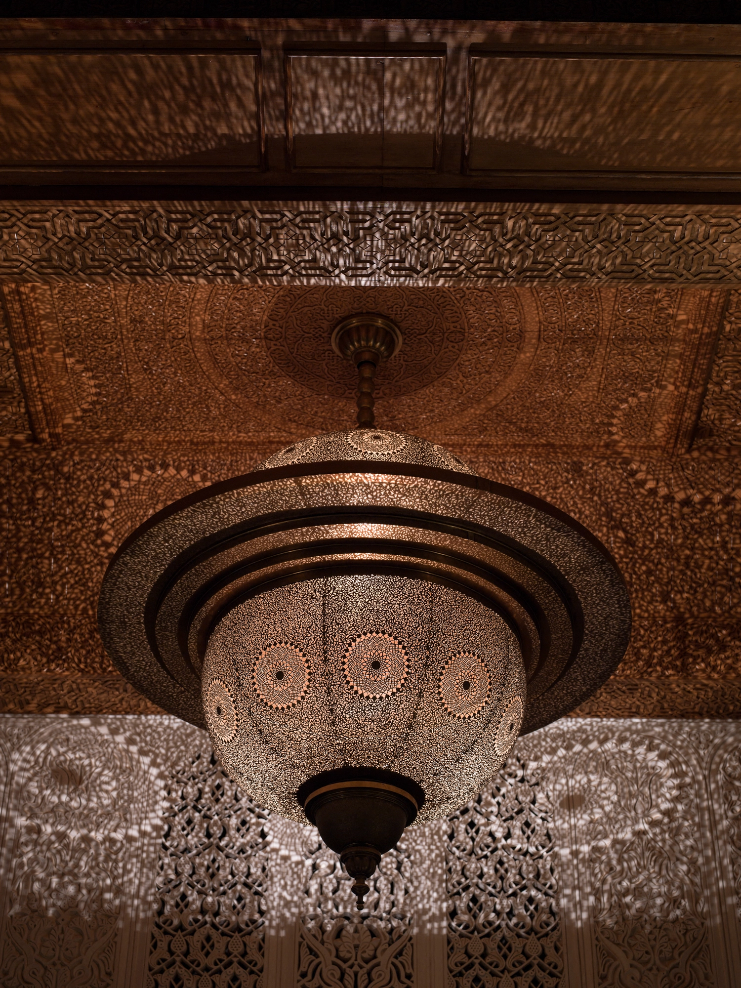 Close-up of a pierced concentric twin-dome pendant light beneath a carved wooden ceiling.