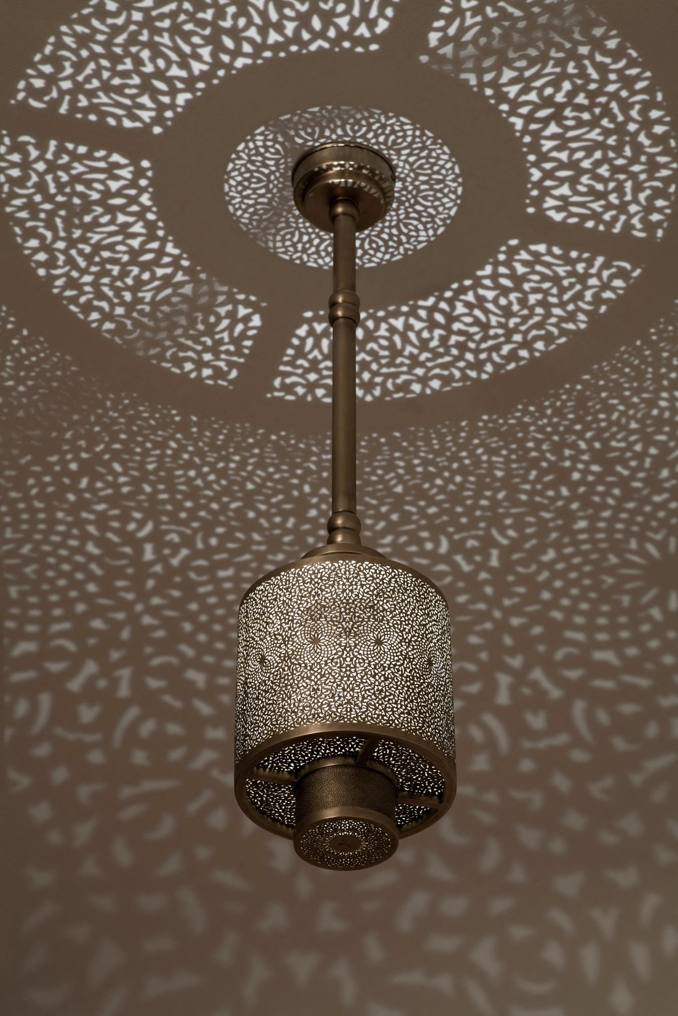 Pierced-brass cylinder pendant on a stem, casting a wide radiating ring of light dots across the ceiling.