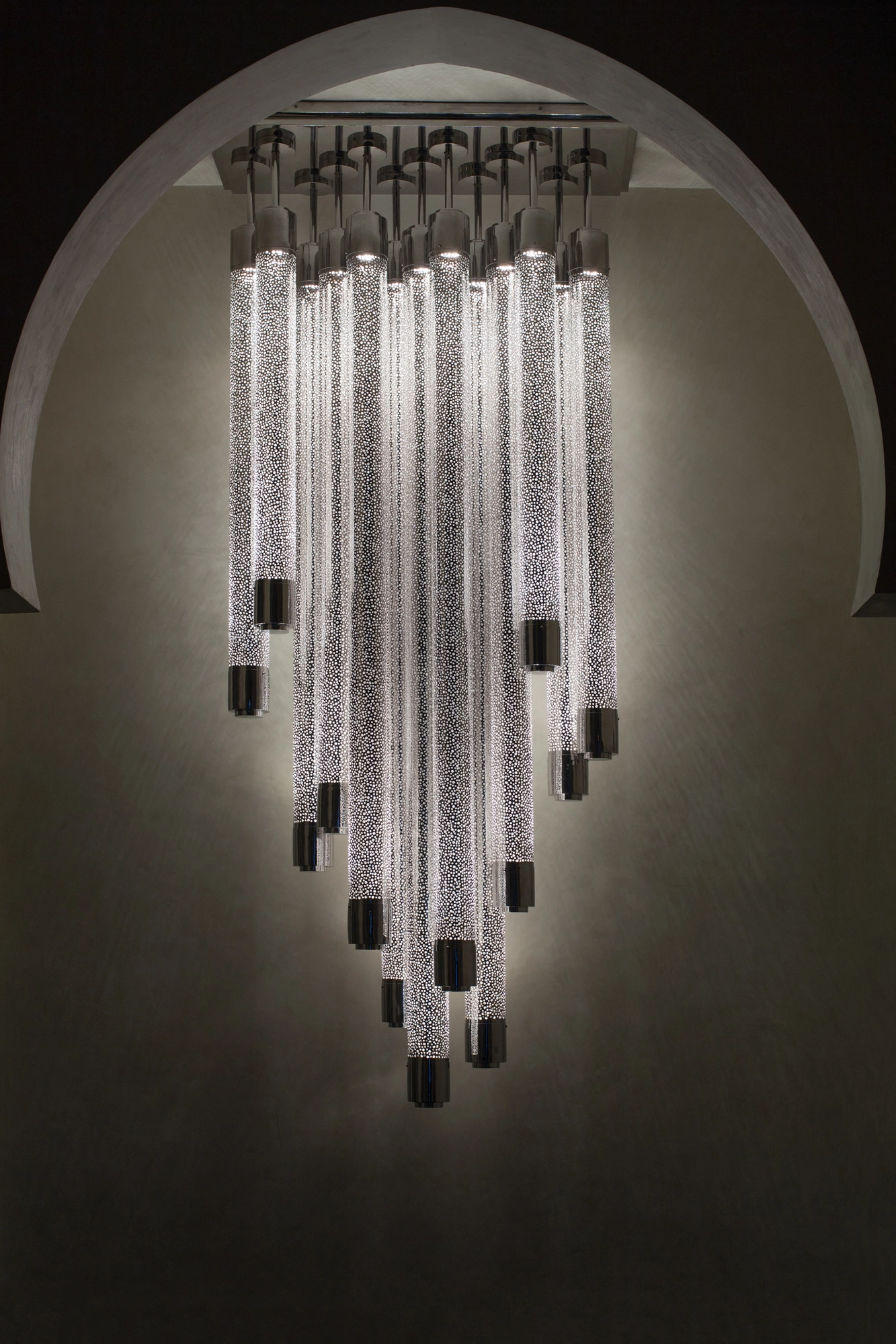 Cluster of cylindrical liquid-light tubes suspended in an arched niche against a dark background.