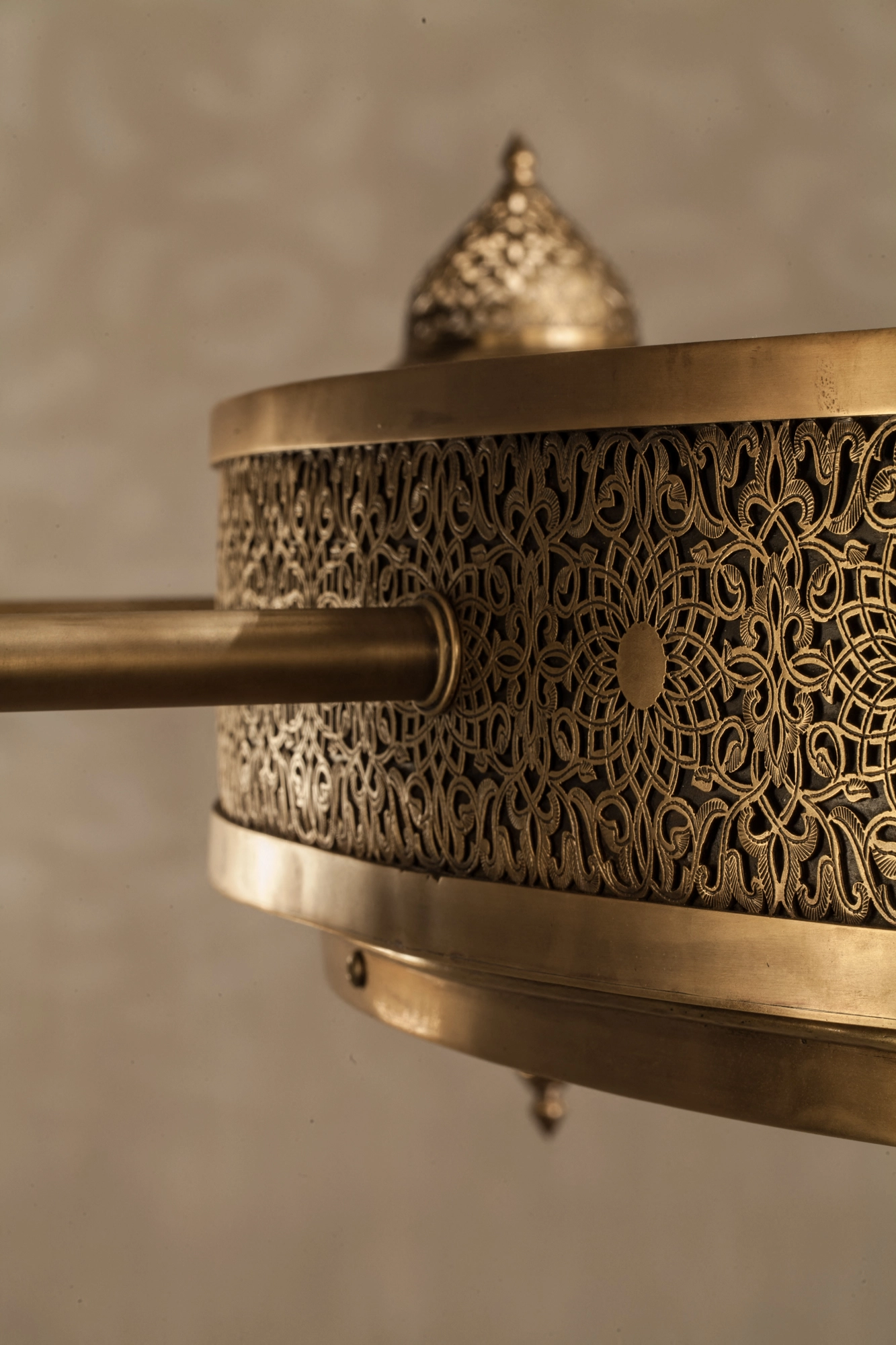 Close-up of the pierced brass crown and rim of a large chandelier, with a domed finial at the top.