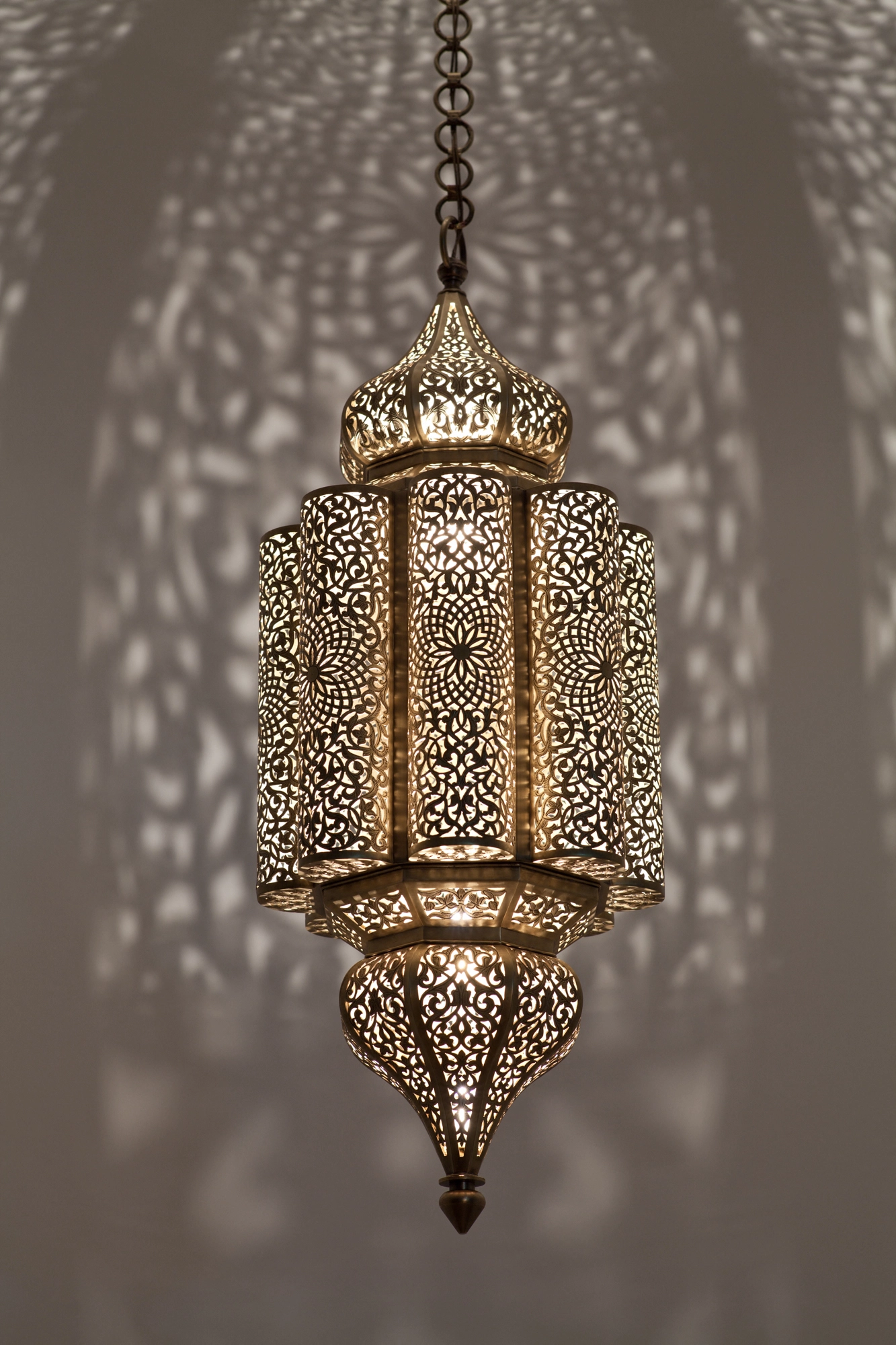 Elongated pierced-brass Andalous pendant lantern glowing amid a dense scatter of floral light projections on the walls.