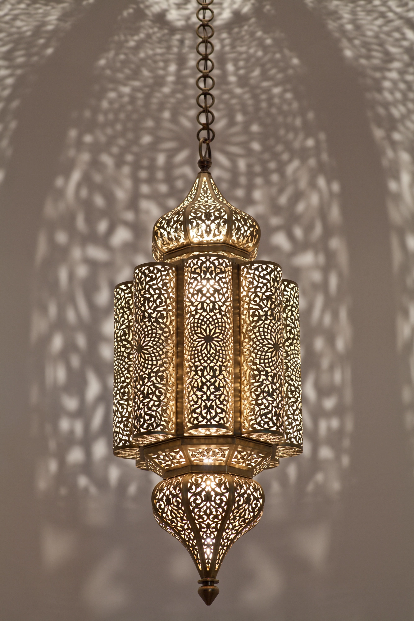 Pierced-brass Andalous lantern lit from within, throwing a symmetrical floral light-and-shadow pattern across the ceiling.