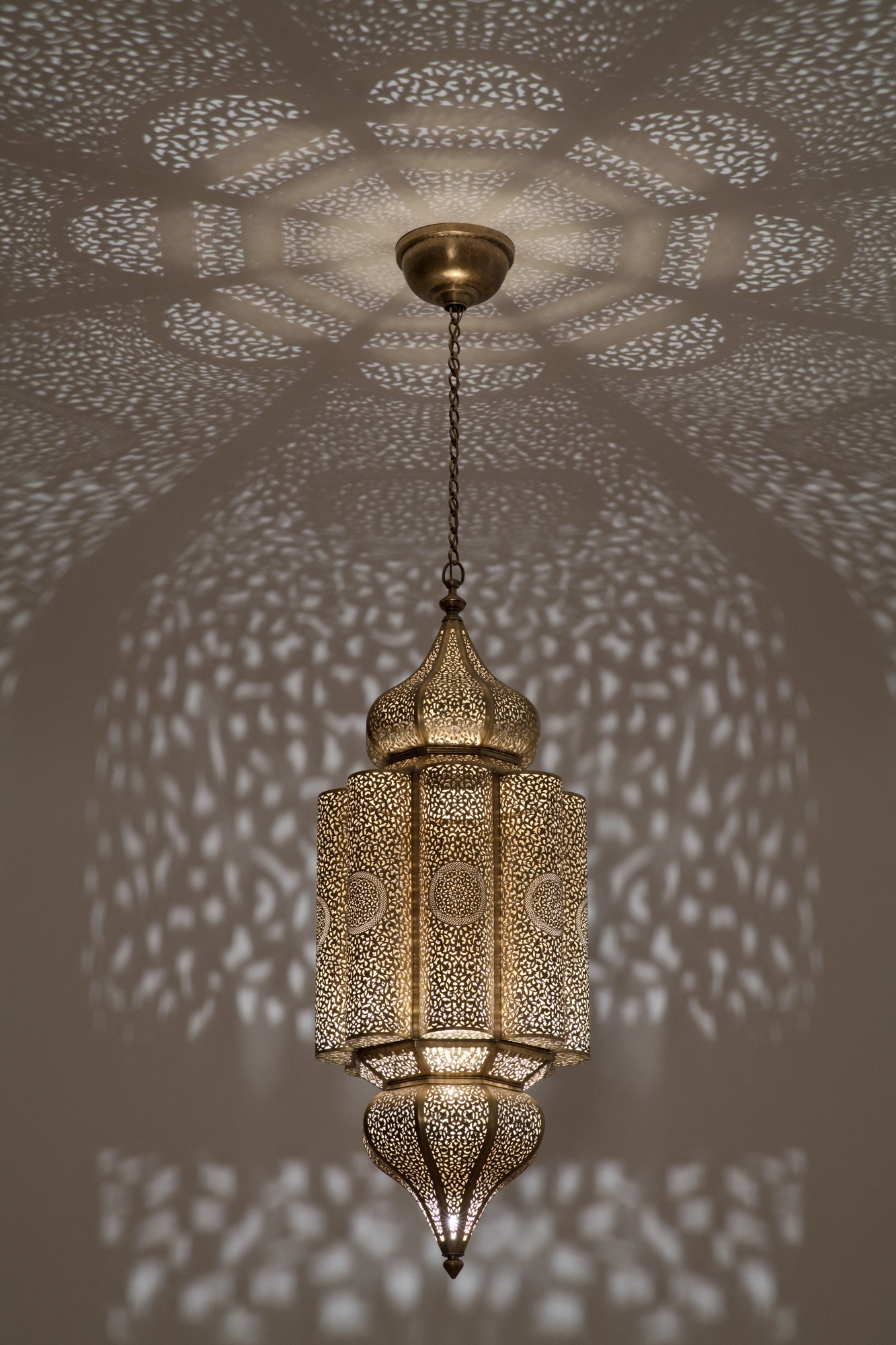 Pierced-brass Andalous pendant lantern viewed from below, casting a radiating circular burst of light dots on the ceiling.