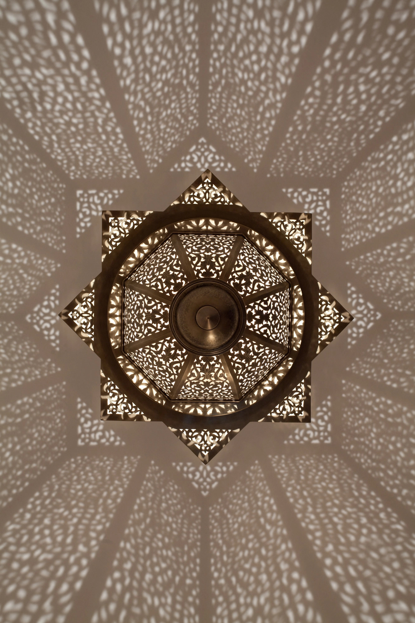 Eight-point pierced star ceiling medallion with a hanging lantern at its center, radiating a dense light pattern.