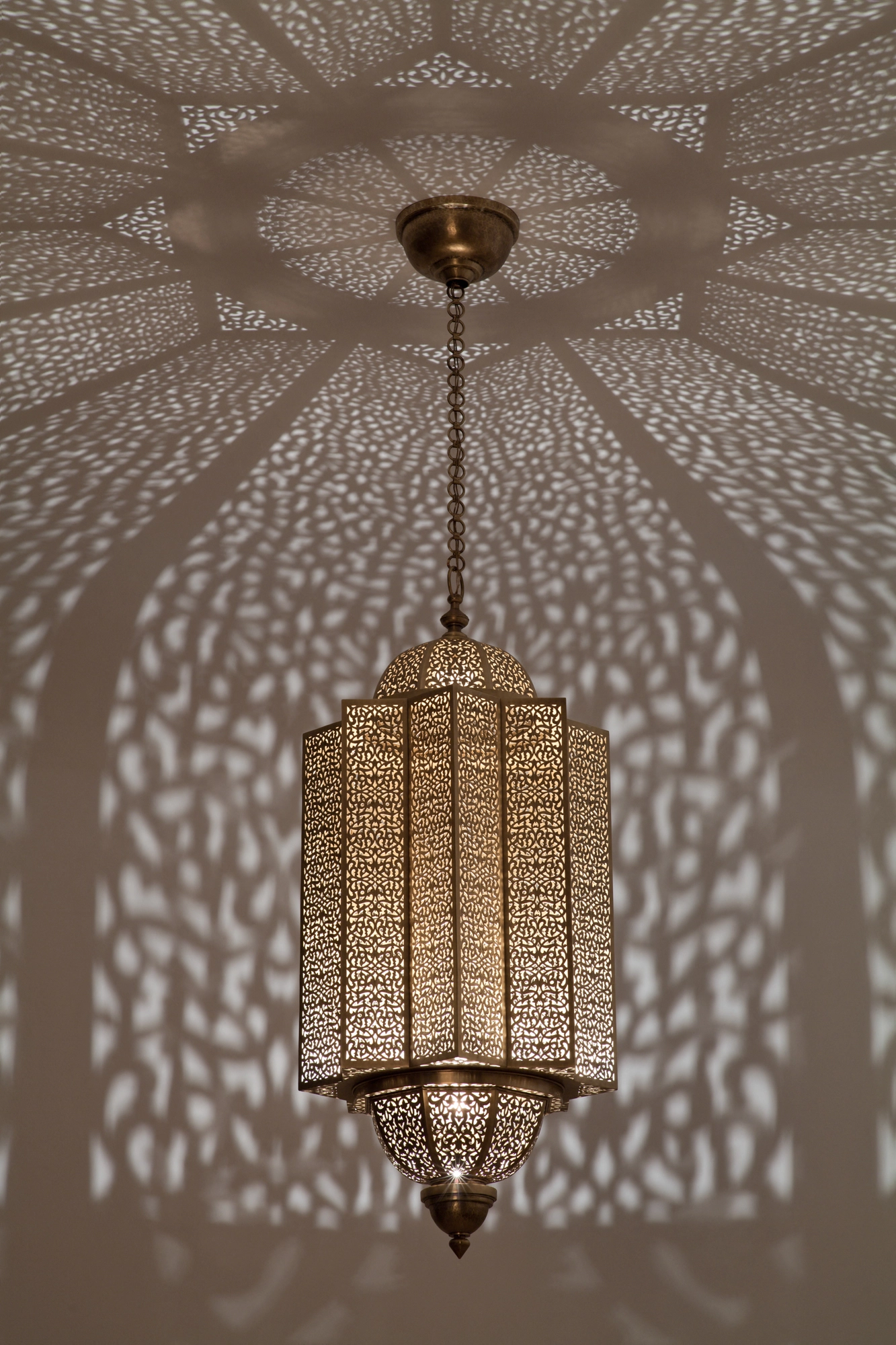 Pierced-brass Moorish lantern suspended beneath a ceiling lit with a large symmetrical starburst of light dots.