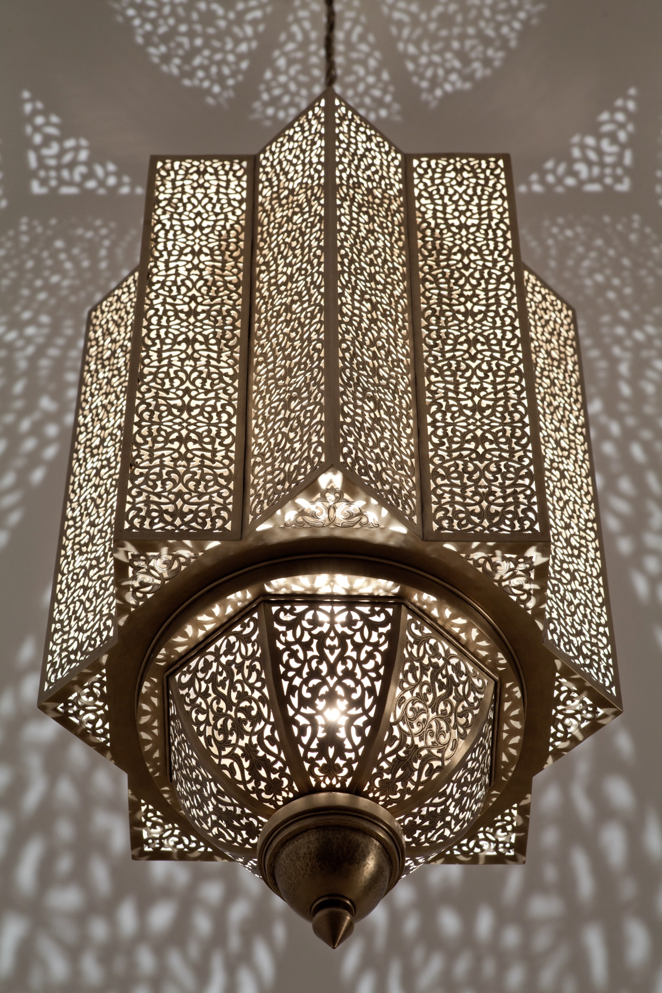 Tapered hexagonal pierced-brass Moorish lantern glowing against a wall scattered with fine light dots.