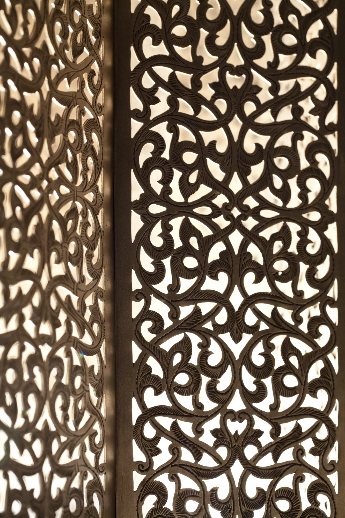 Close-up of a pierced-brass panel with glowing arabesque scrollwork against deep shadow.