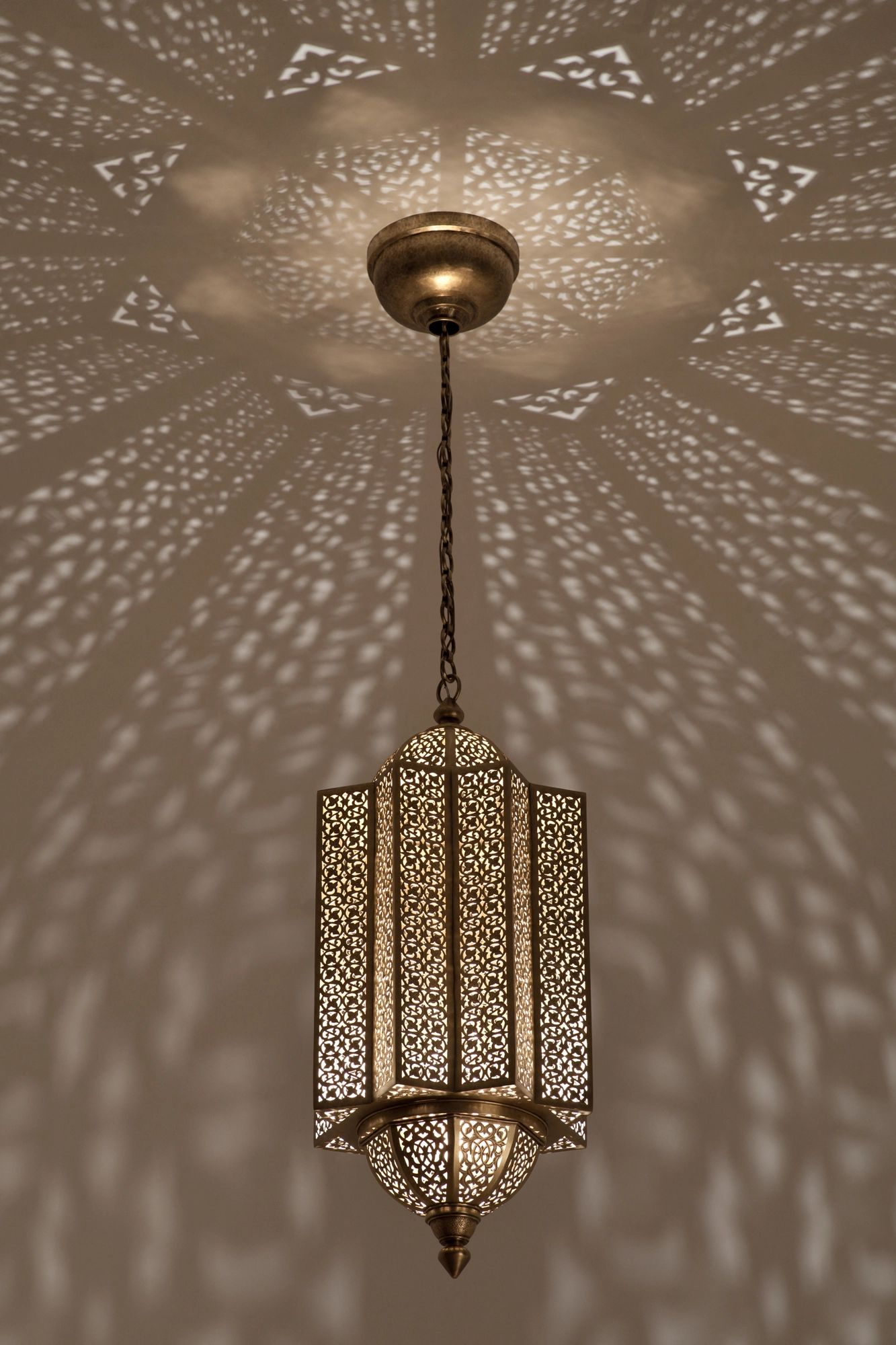 Pierced-brass Moorish lantern on a chain, casting a wide radiating burst of light across the ceiling.