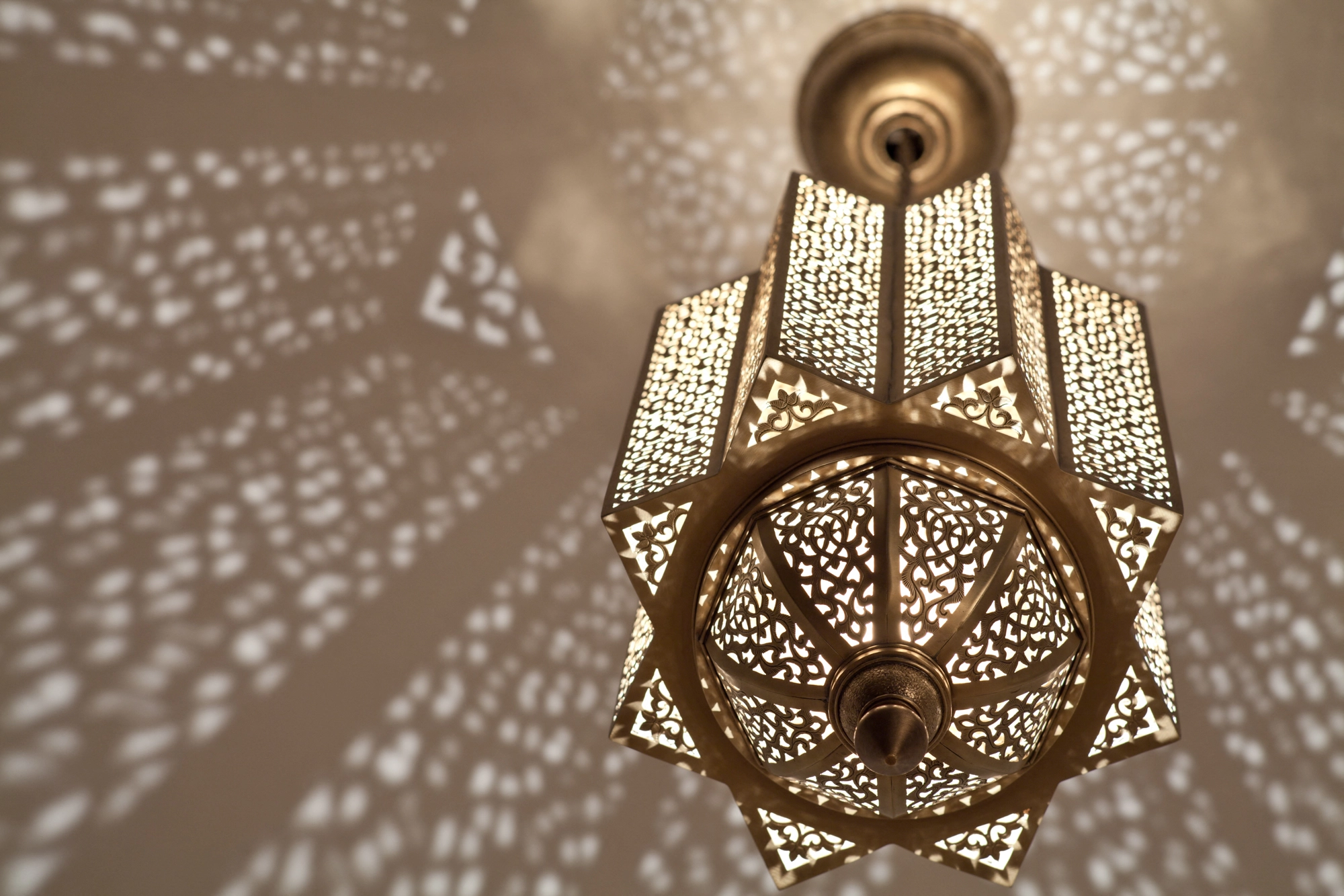 Pierced-brass Moorish lantern with a circular wheel base, glowing softly amid scattered ceiling light.