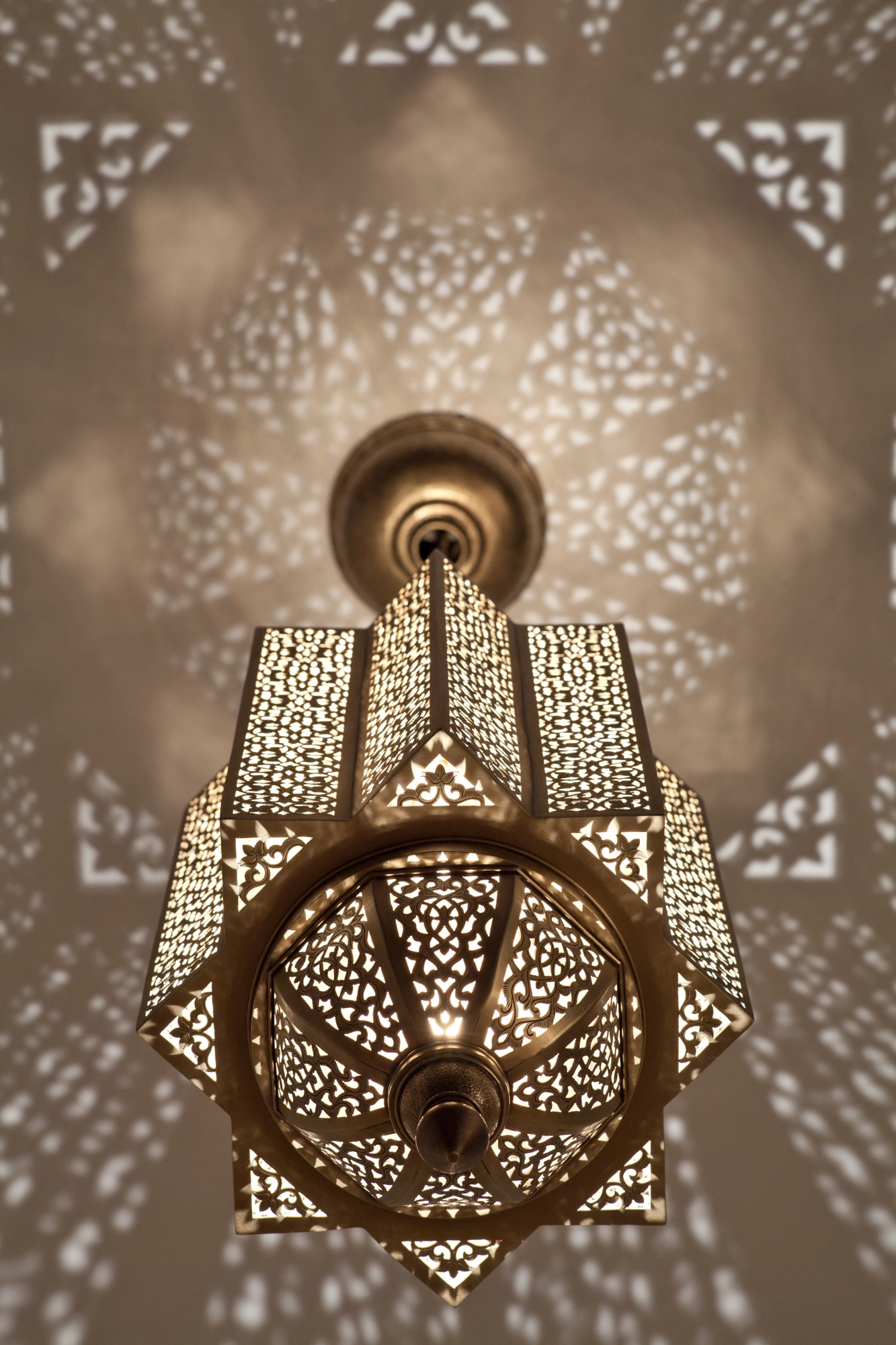 Hexagonal pierced-brass Moorish lantern with a wheel-form base, glowing within a star-shaped light pattern.