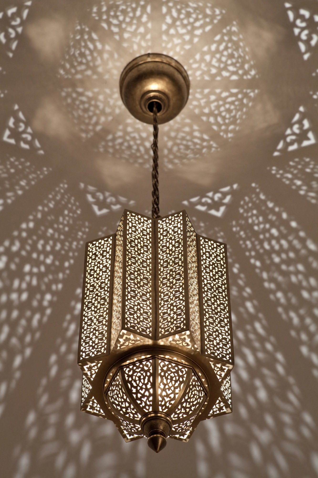 Pierced-brass Moorish pendant lantern glowing beneath a ceiling scattered with a symmetrical light pattern.