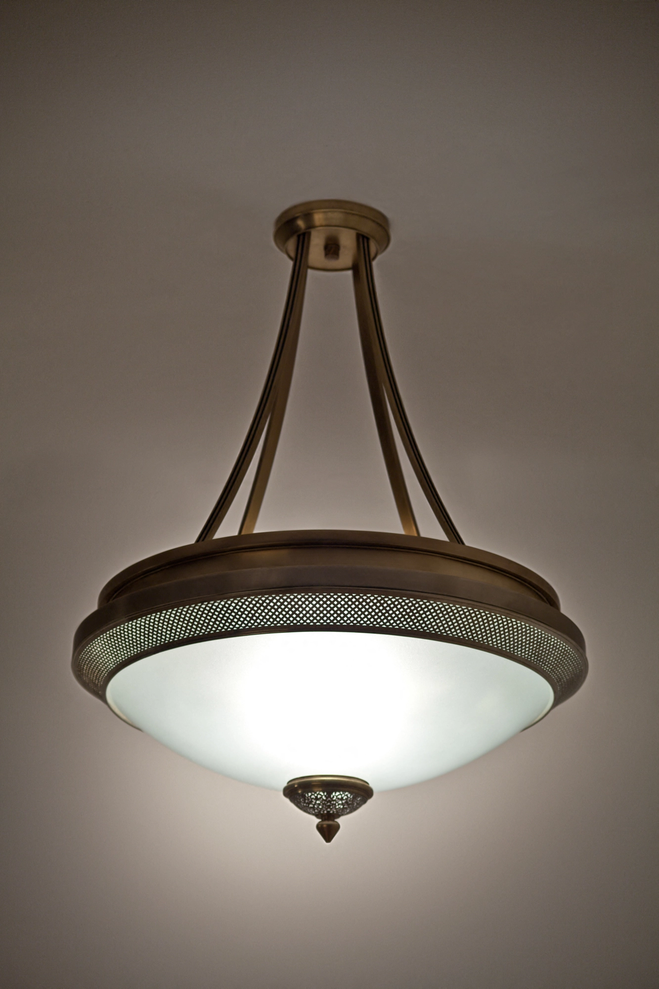 Sofia pendant with a white glass bowl in a pierced-brass three-arm cradle, lit softly beneath a pale ceiling.