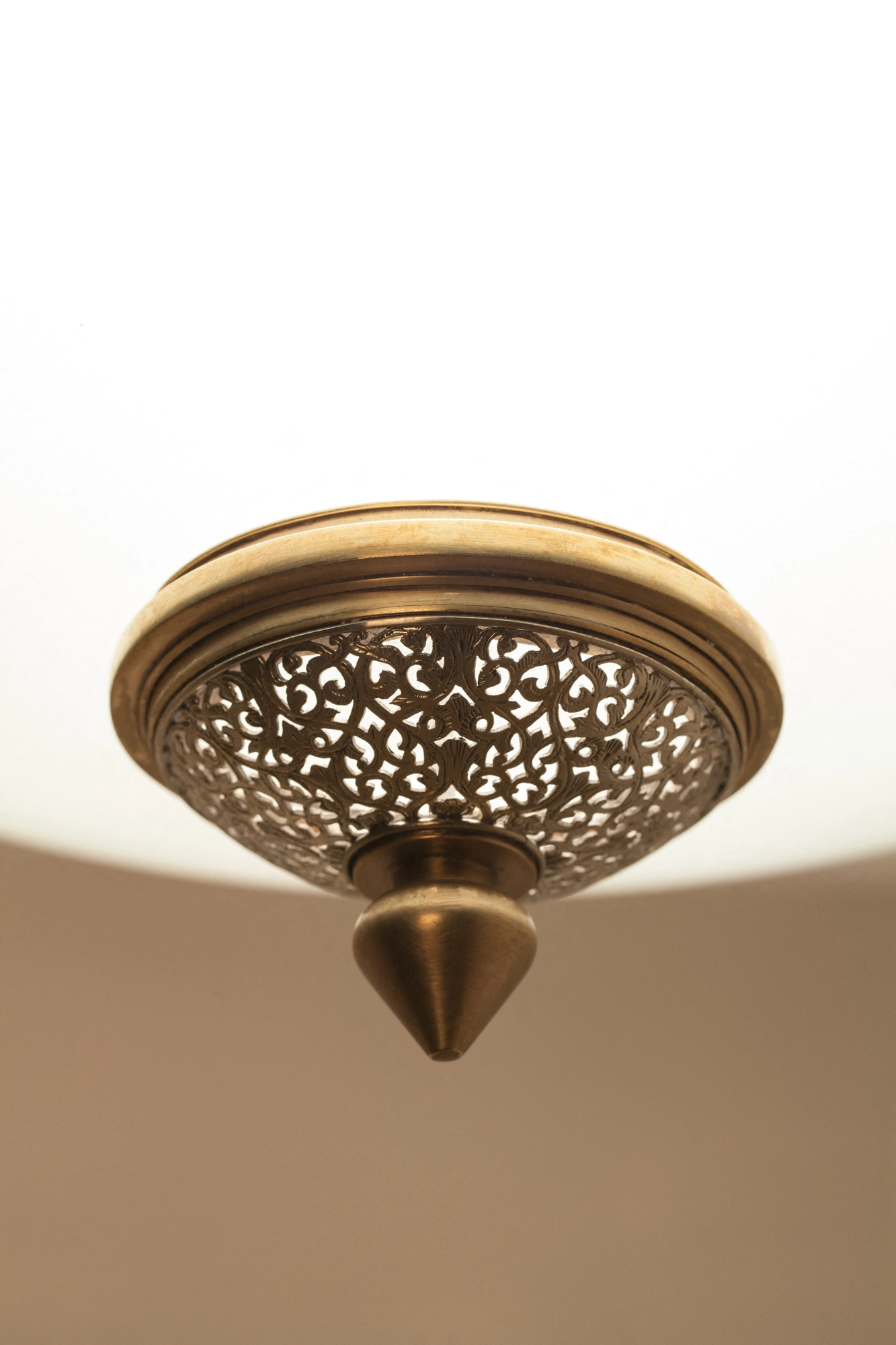 Close-up of a Sofia pendant's pierced-brass domed cap and pointed finial, glowing against a warm ceiling.