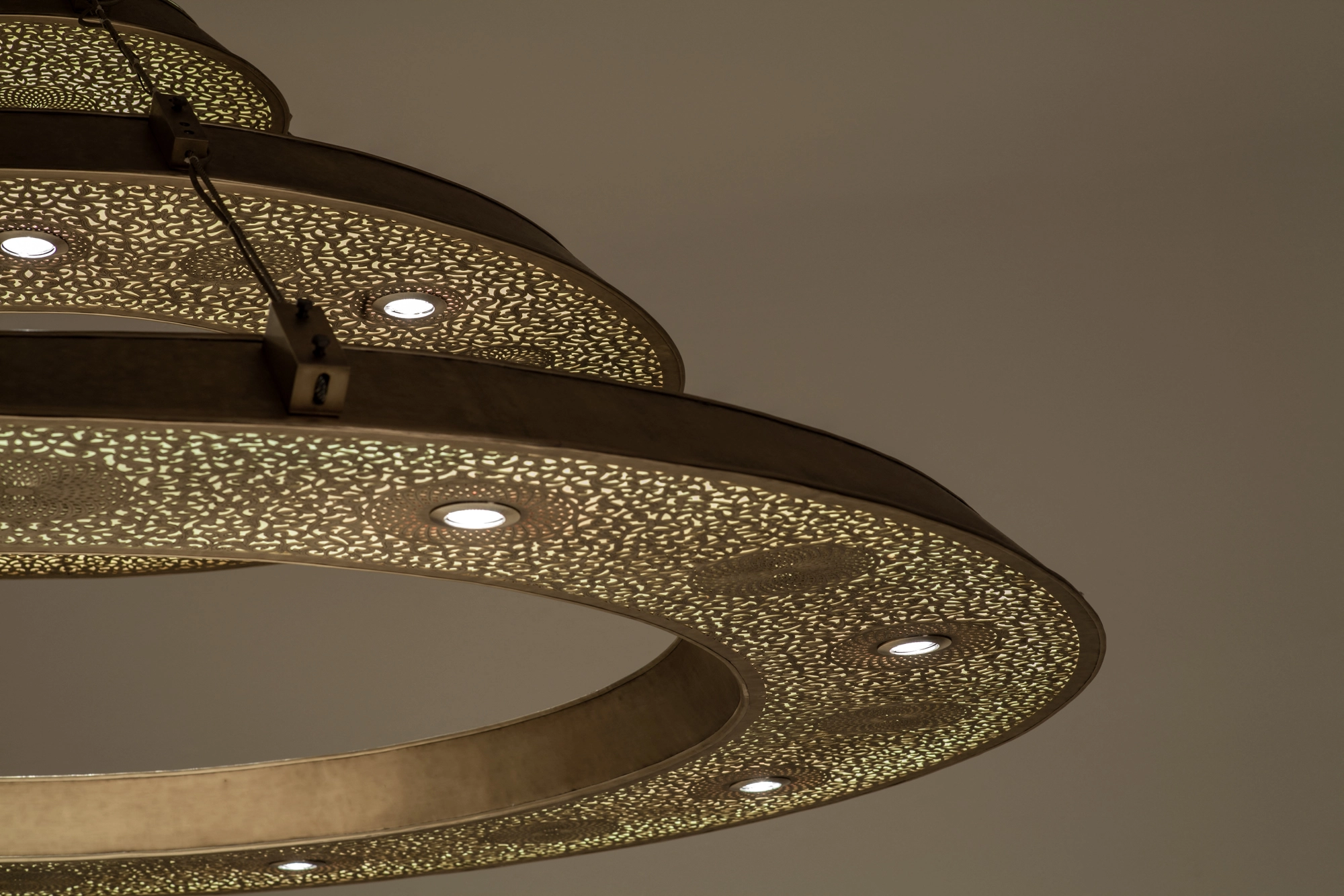 A triple-ring pierced metal chandelier seen from below, scattering dotted light through its perforations.