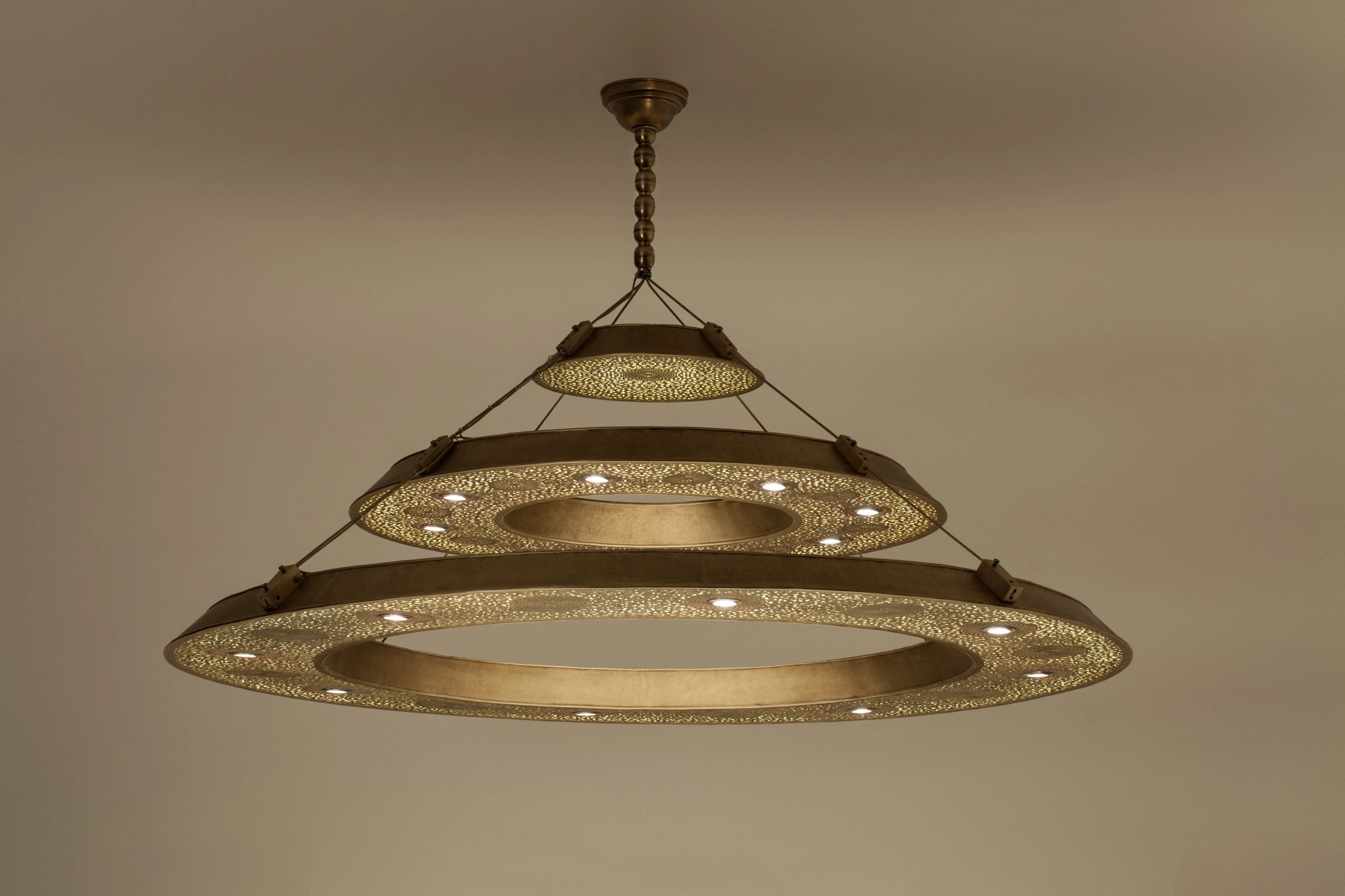 A chandelier of three stacked pierced metal rings suspended from the ceiling, glowing warmly.