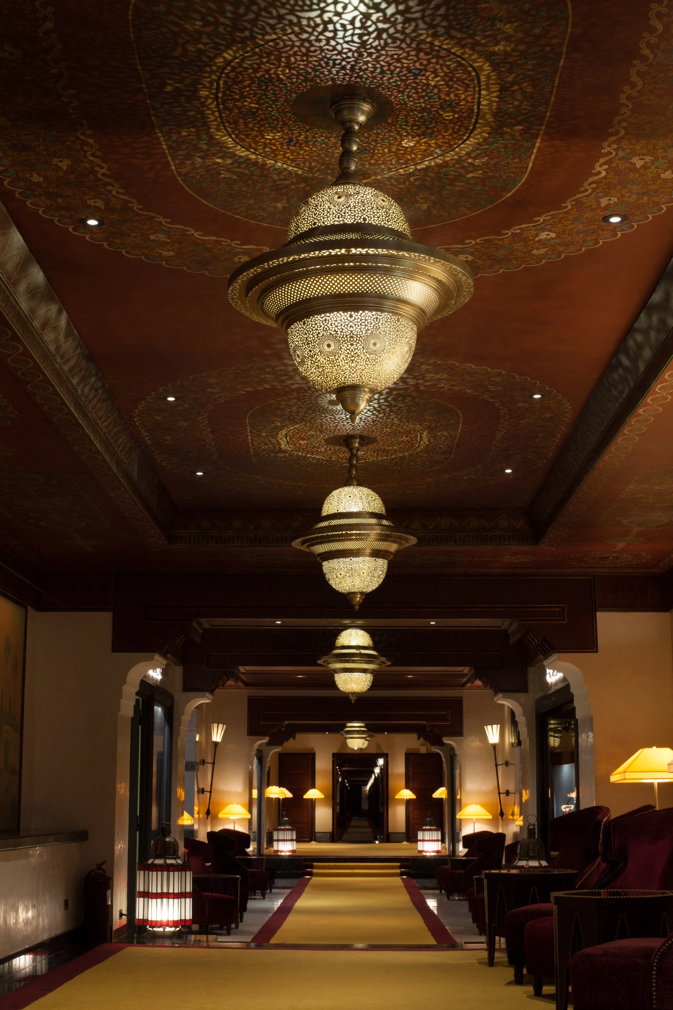 Tiered pierced twin-dome chandeliers above a long elegant lounge lined with seating.