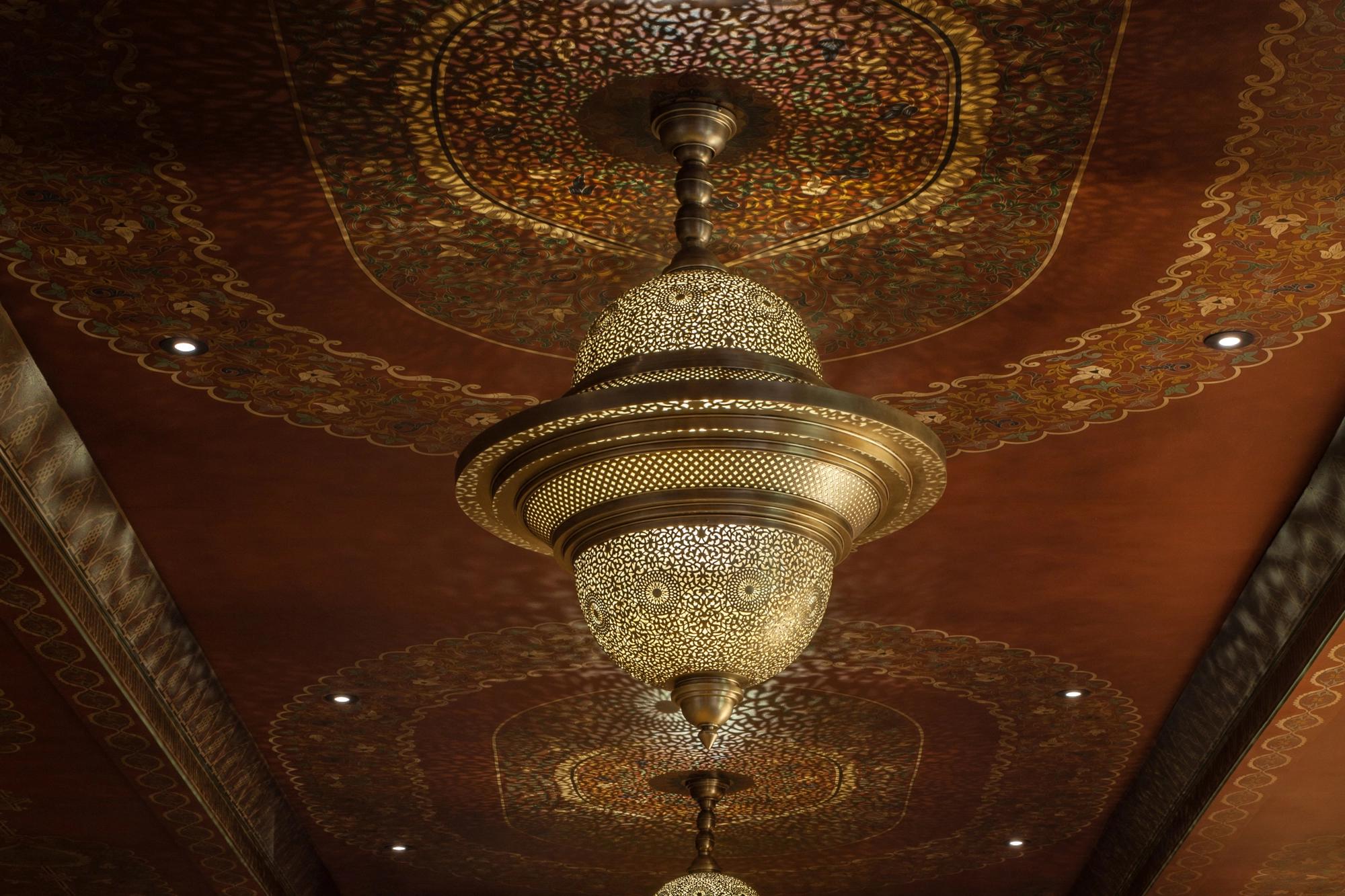 Large tiered pierced twin-dome chandelier glowing beneath an ornate gilded ceiling.