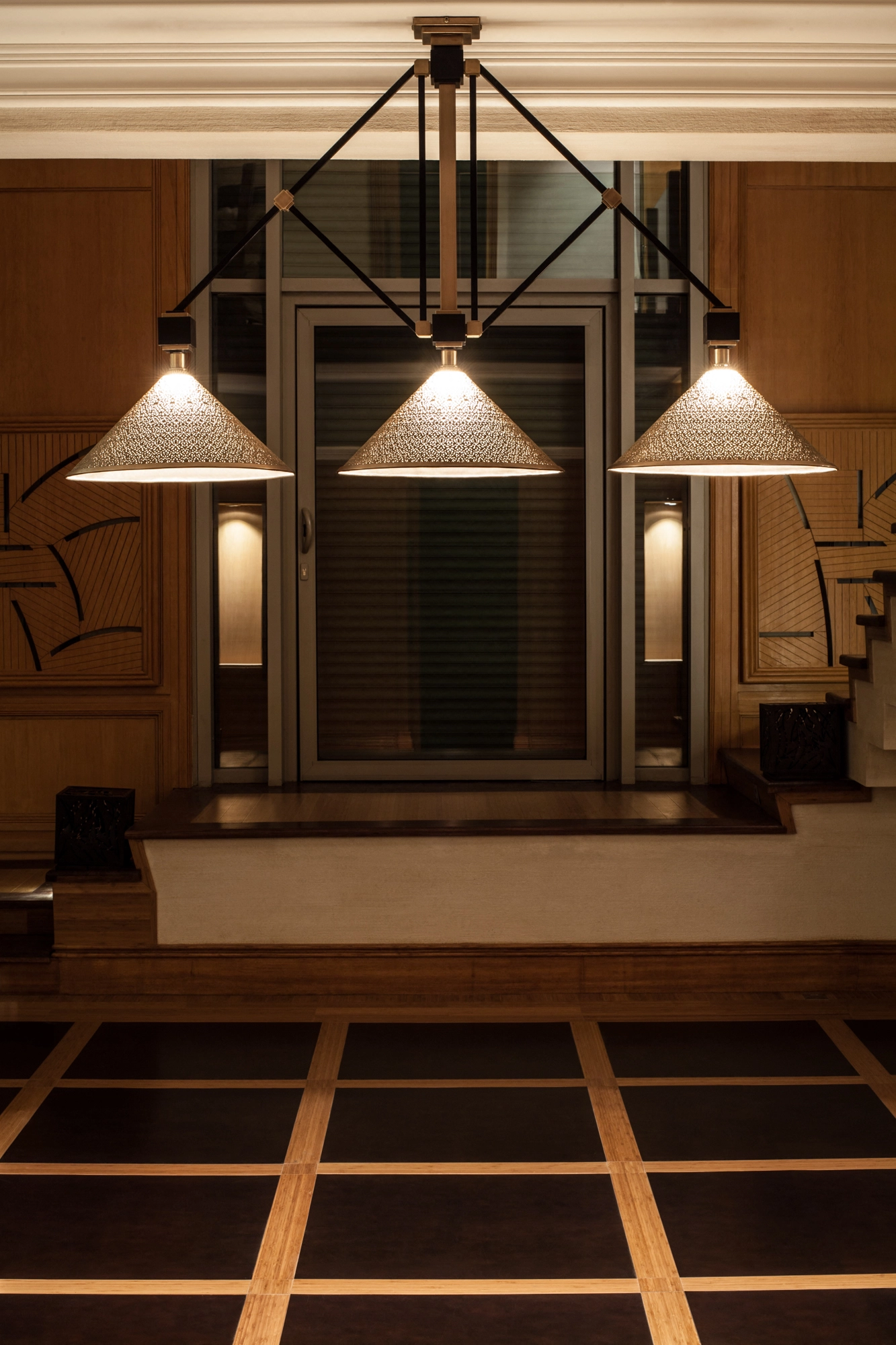 Three conical pierced pendant lights glowing warmly above a panelled doorway in a dim room.