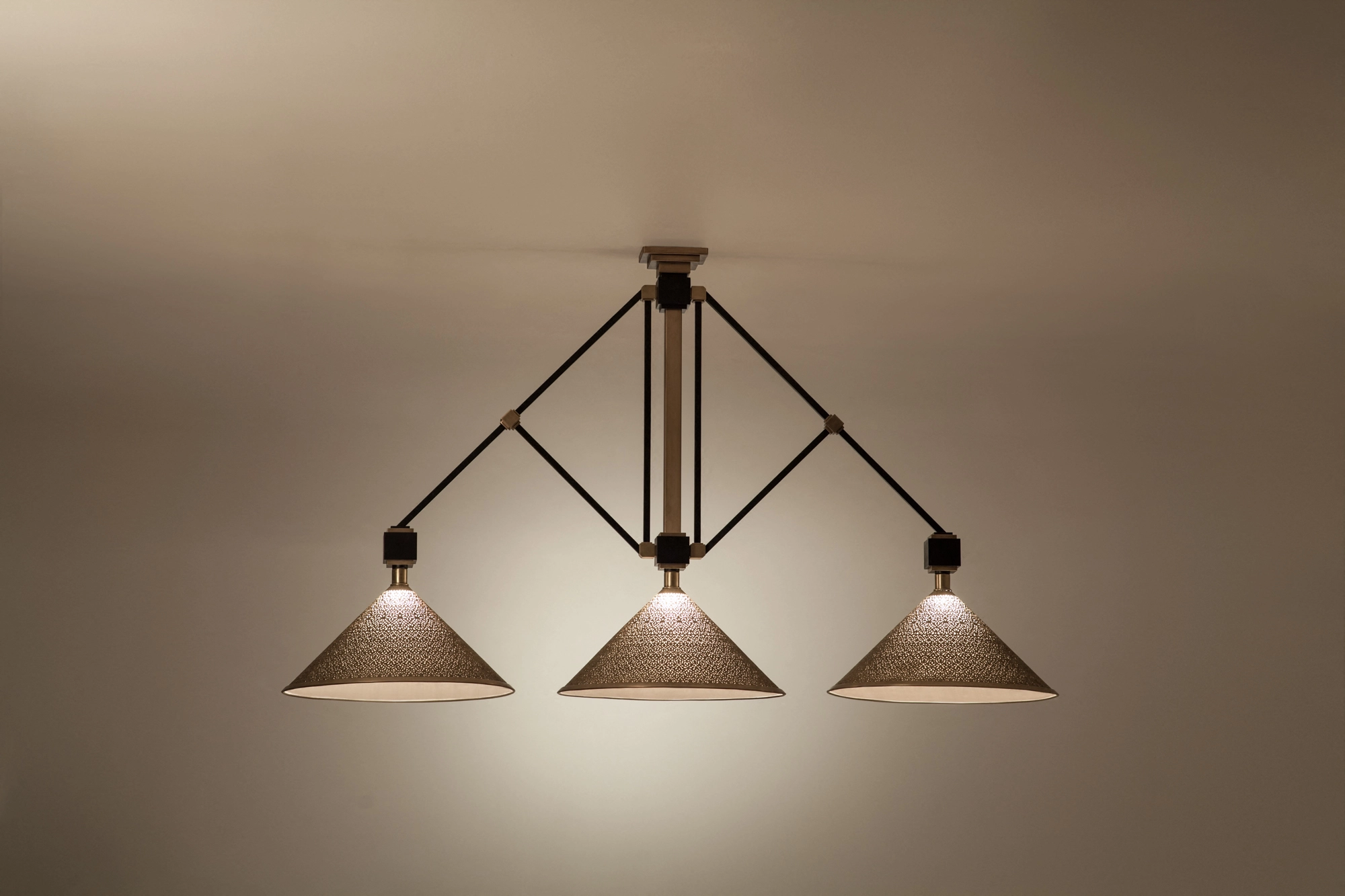 Three conical pierced pendant shades on a dark frame, lit warmly and seen close from below.