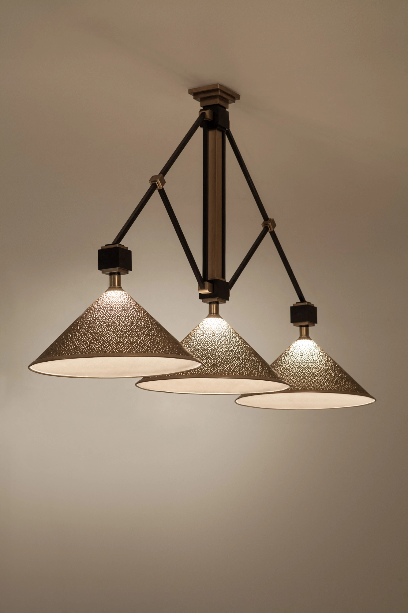 Three conical pierced pendant shades on a black rod frame, suspended from the ceiling and glowing warmly.