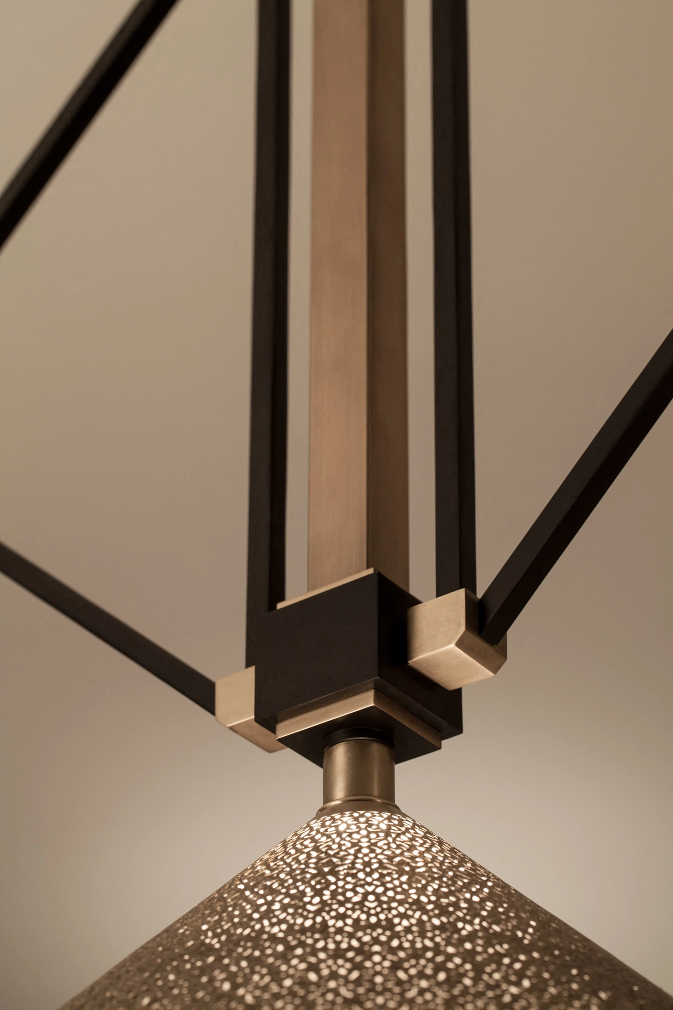 Close-up of a pierced conical pendant shade and the black rod joint suspending it.